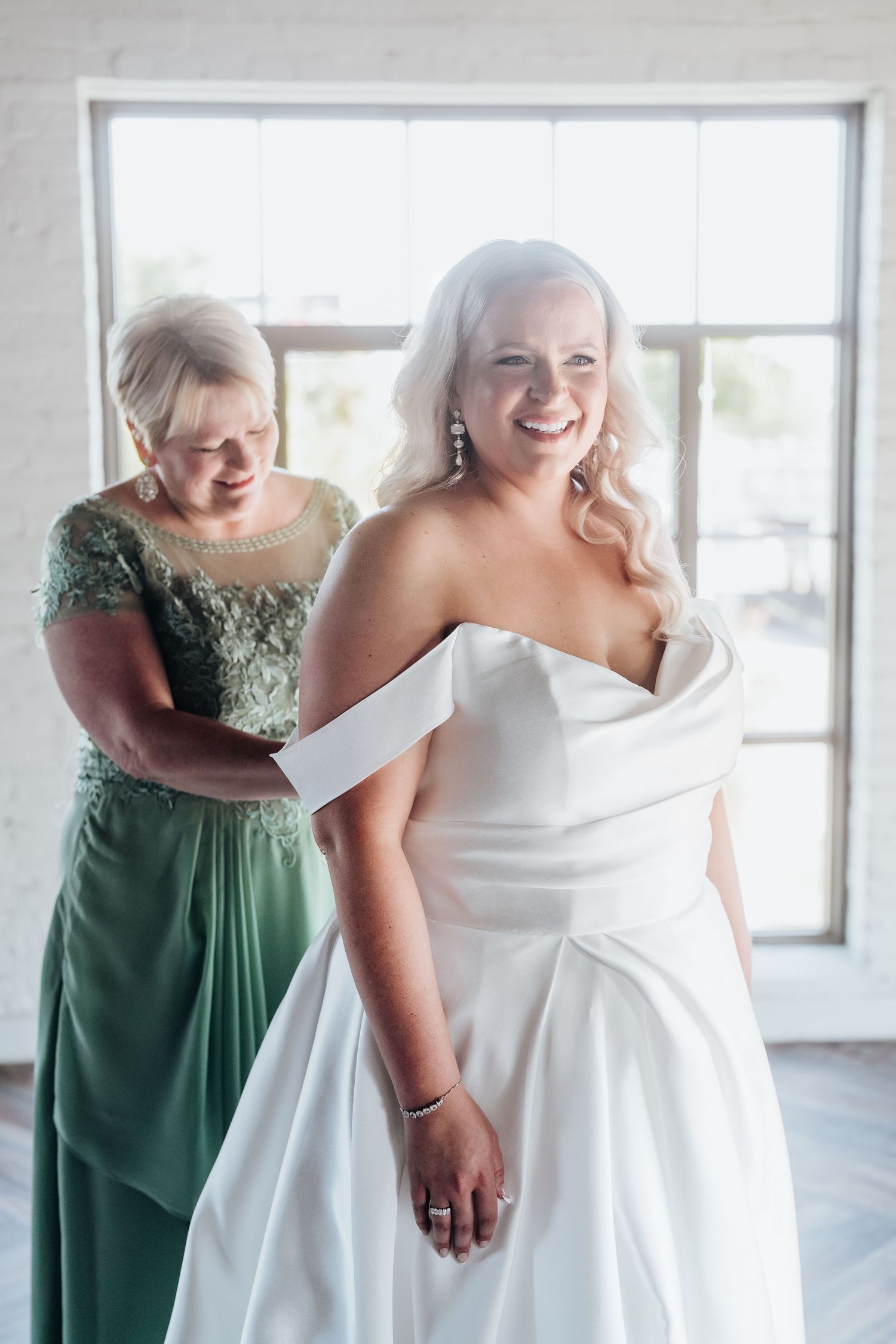 Joyful wedding party moment with bridesmaids in sage green dresses celebrating together.