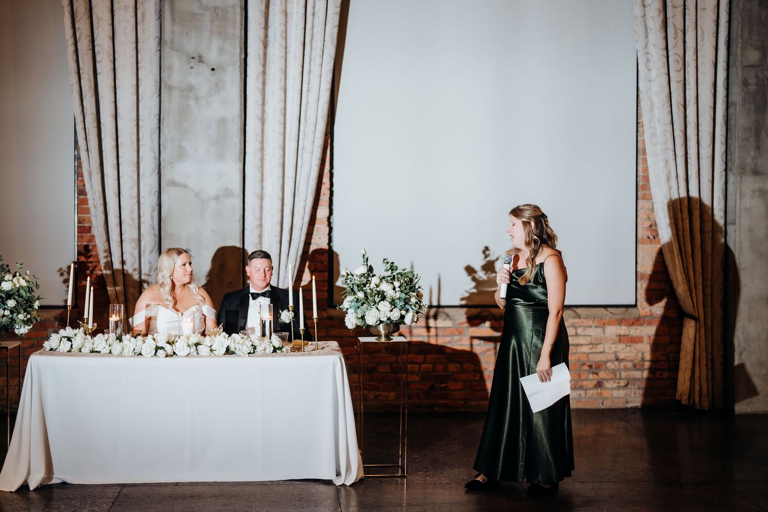 Wedding reception setup in an industrial-chic venue with white linens and exposed brick walls.