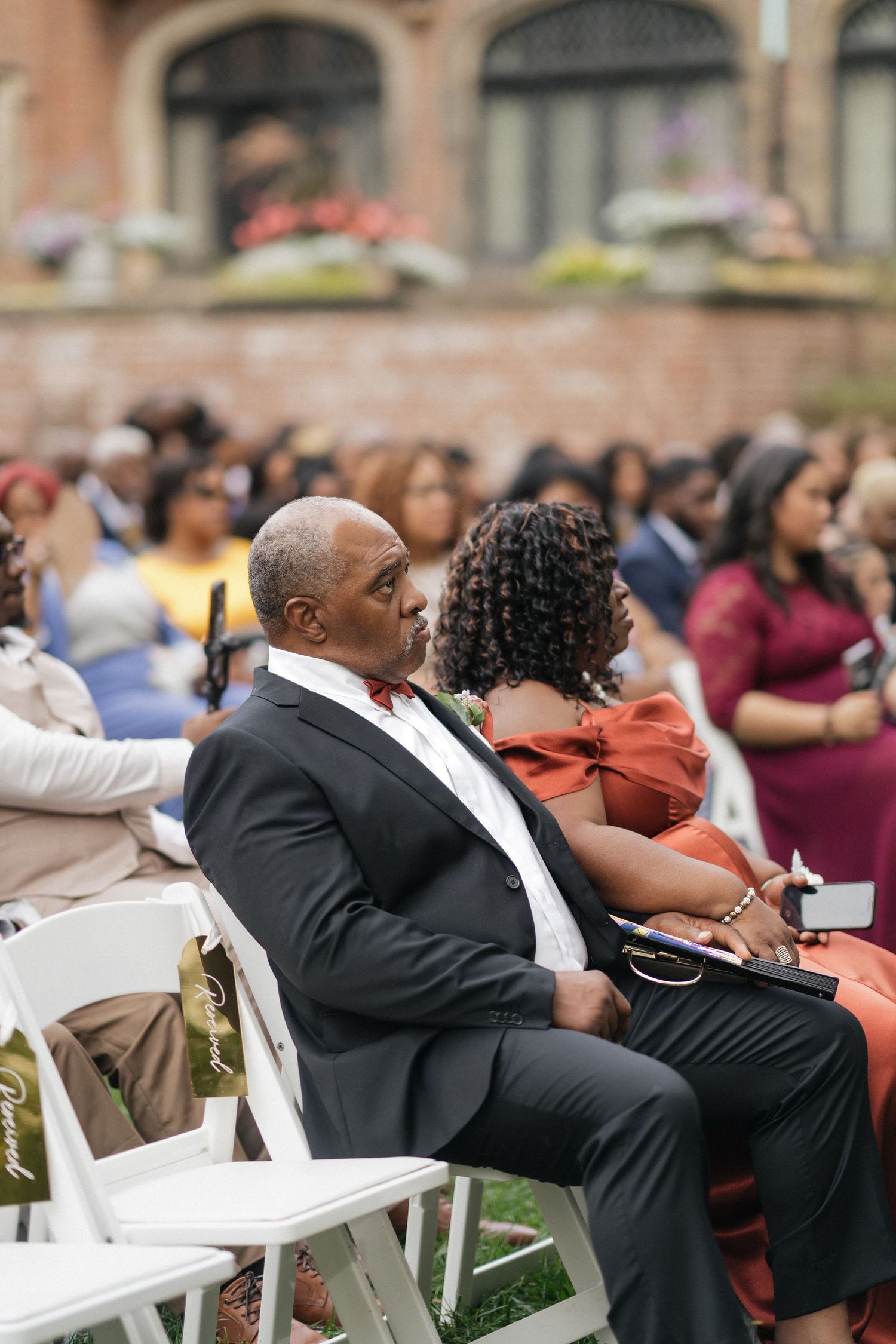 Wedding guests seated in white chairs during an outdoor ceremony.