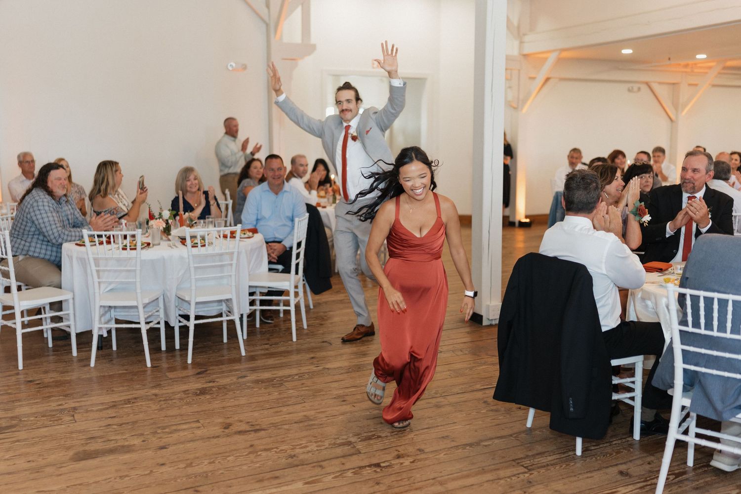 Wedding guests dancing and celebrating in a bright reception hall with white decor.