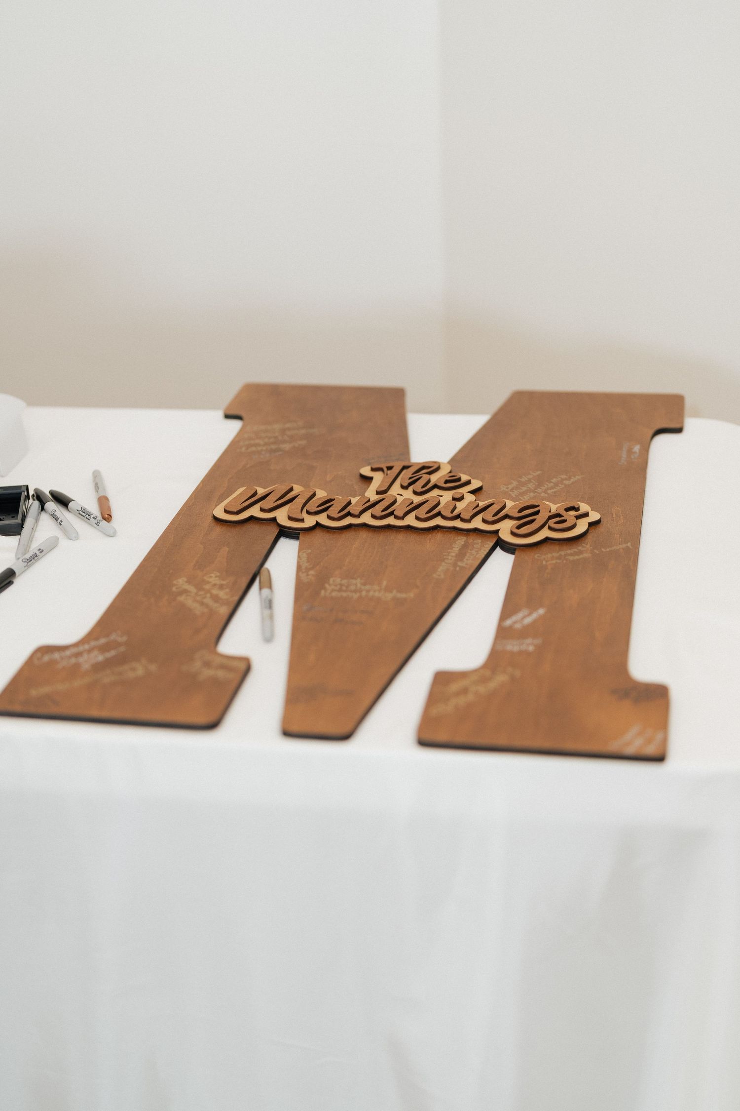 Decorative wooden letter M with cursive writing displayed on white tablecloth.