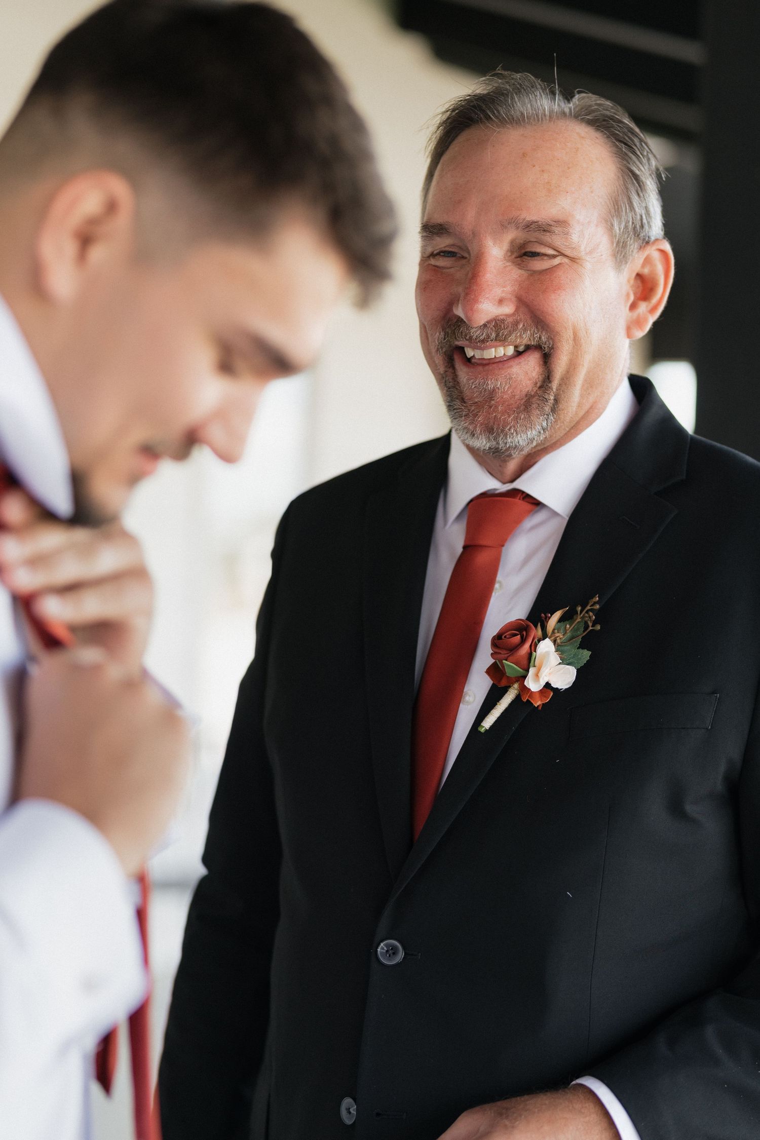 Two people in formal attire share an emotional moment with red accents in their wedding attire.