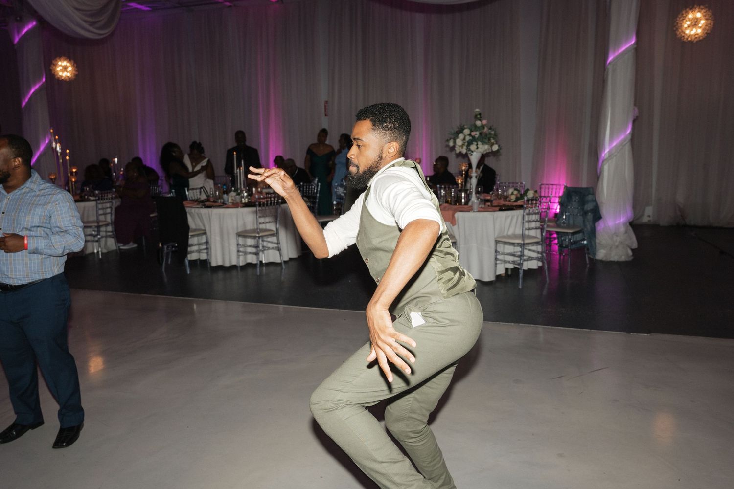 Wedding guest dances energetically on reception dance floor with purple lighting.