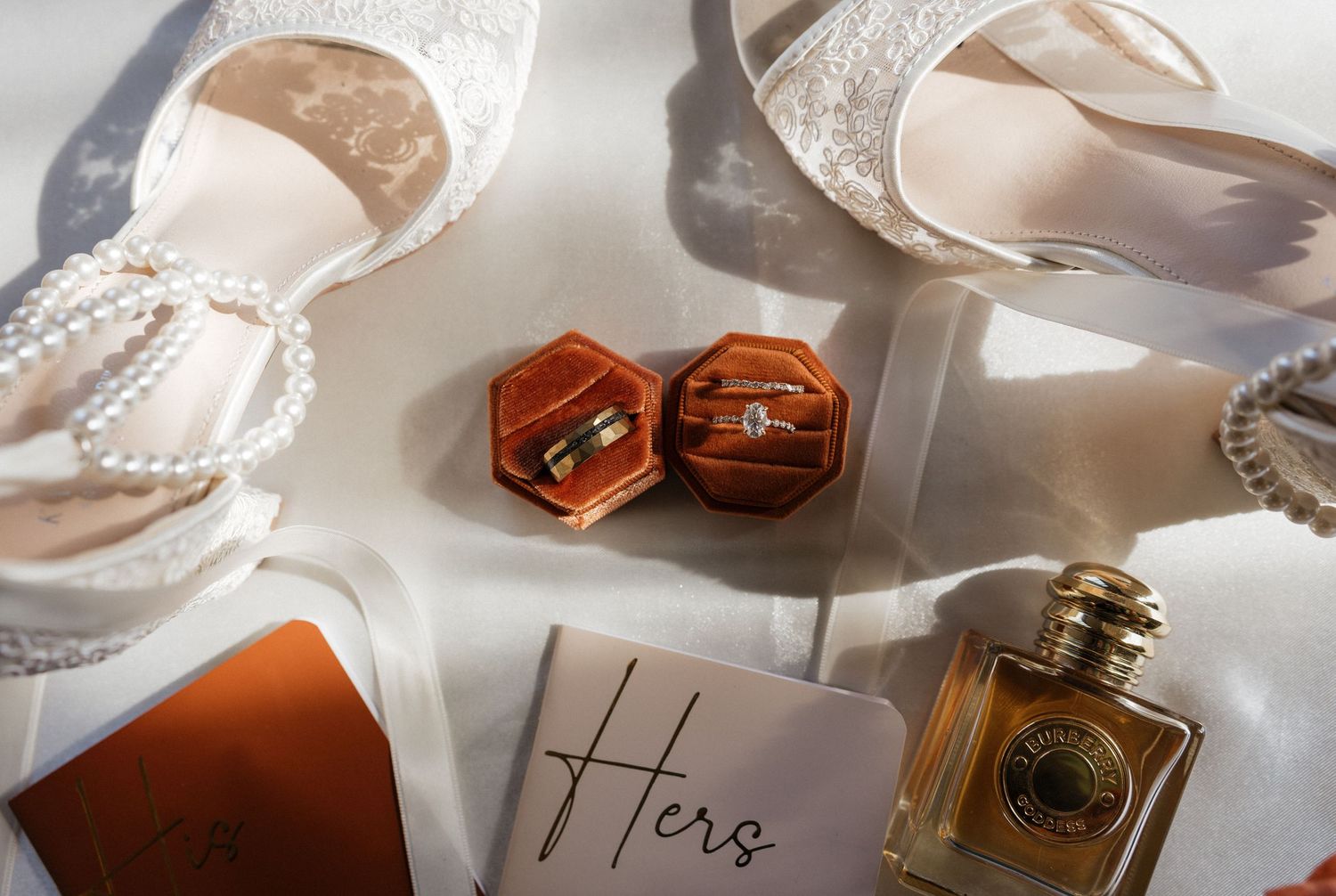 Wedding detail shots of perfume bottles, rings, and delicate accessories arranged on a white surface.