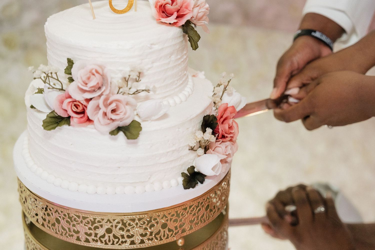 A collection of elegant white wedding cakes decorated with pink roses and gold accents being served at a reception.