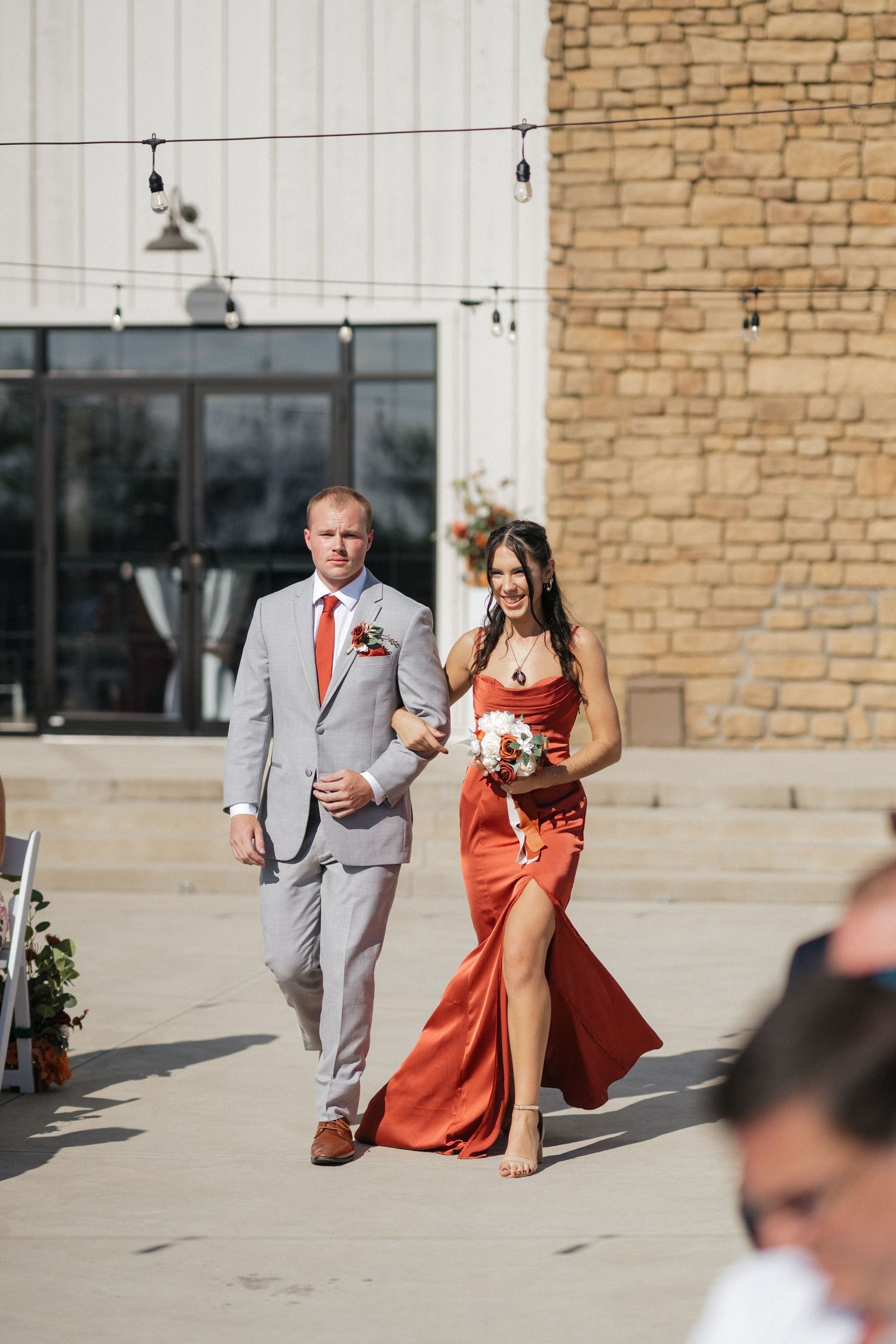 Wedding party members in gray suit and coral dress walking down stone steps.