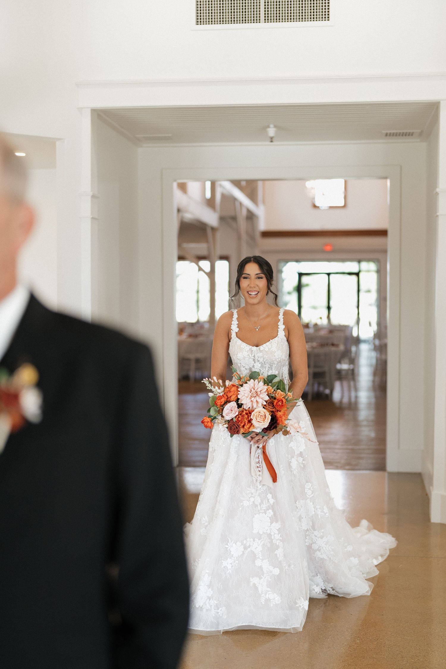 Bride in a white lace wedding dress walking through a bright, modern indoor venue.