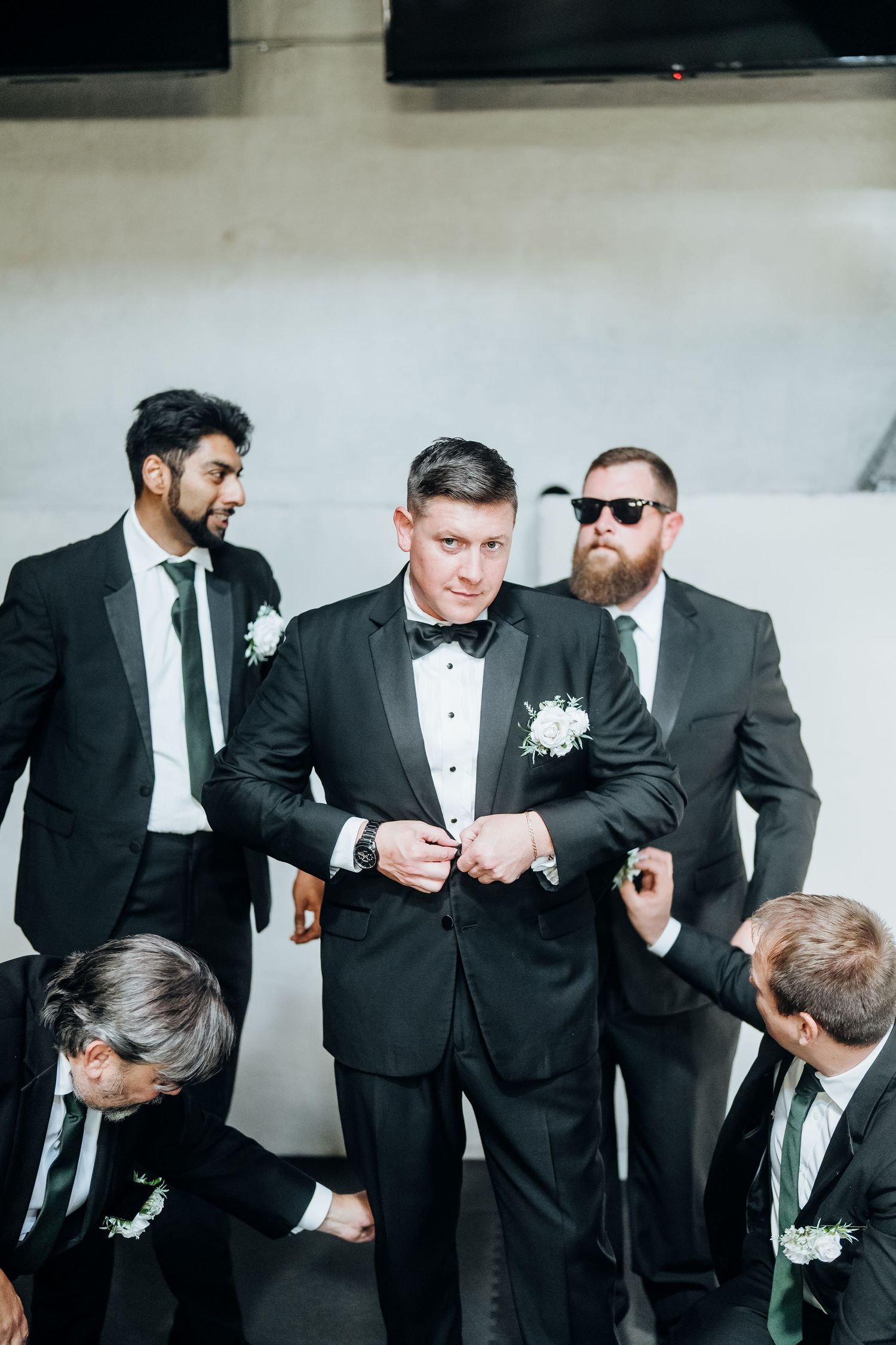 Groomsmen in black suits and ties gather for a candid pre-wedding moment.