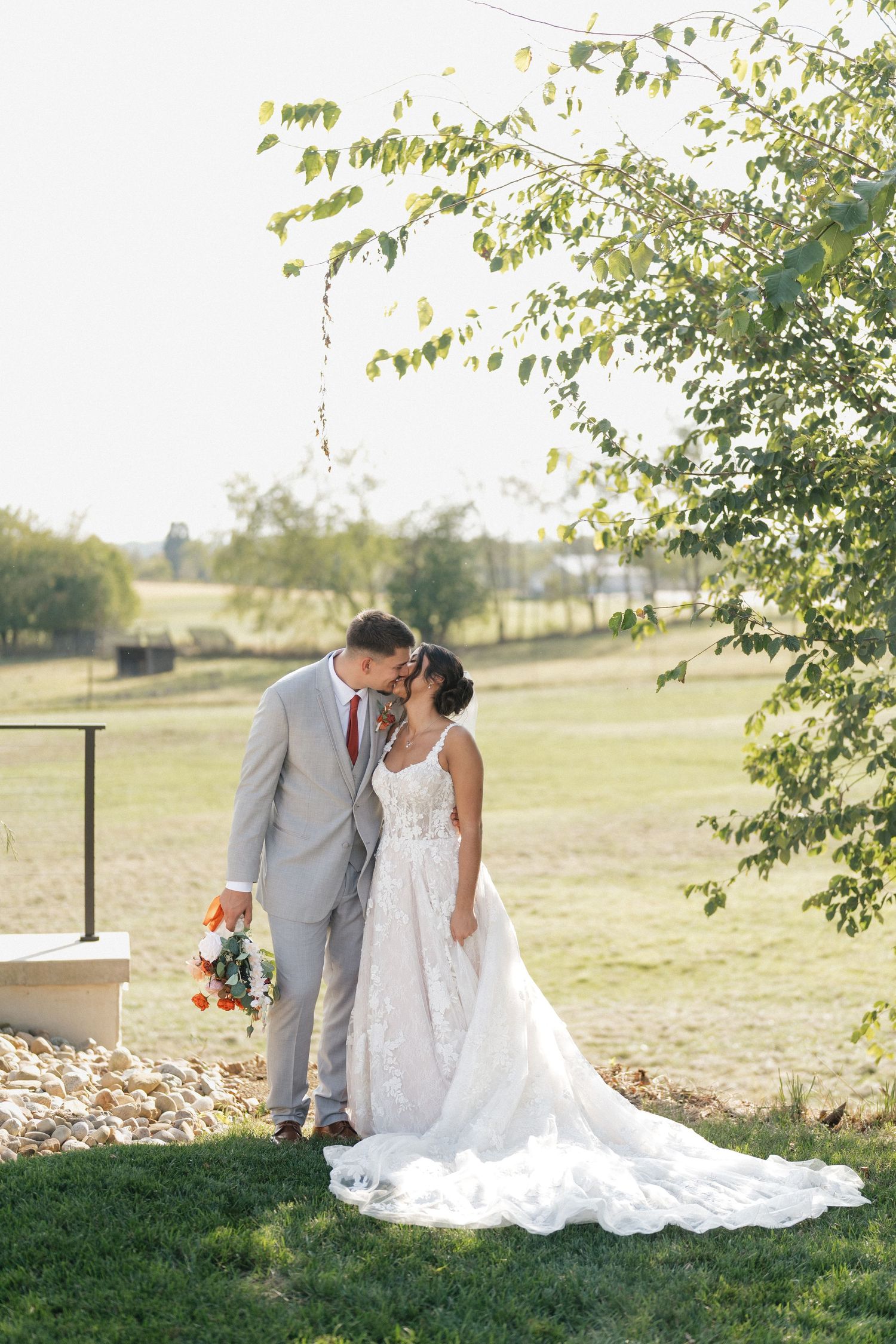 A romantic wedding photo series showing a couple sitting on grass under trees during golden hour.
