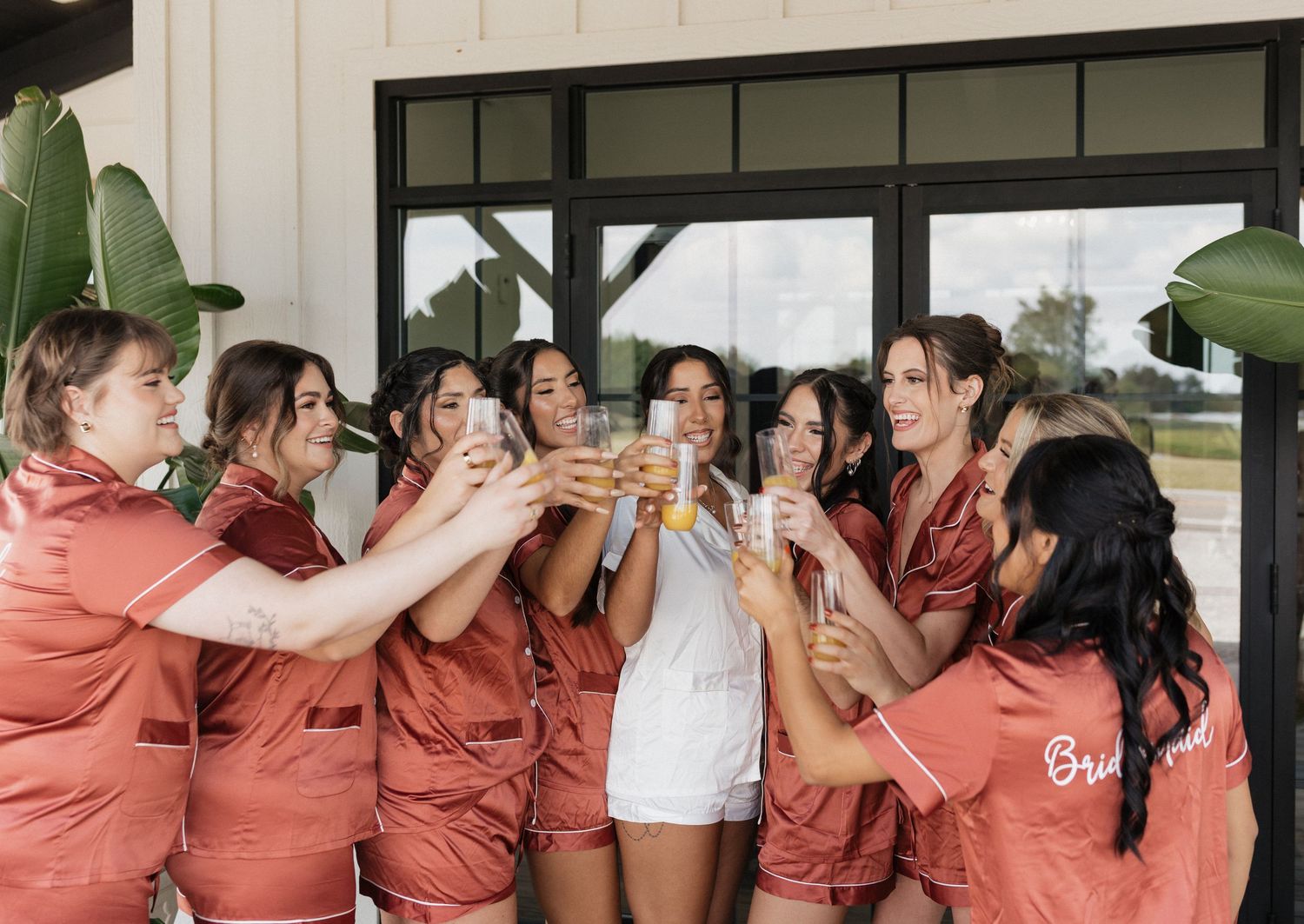 Row of bridesmaids in rose-colored dresses laughing together on a porch.
