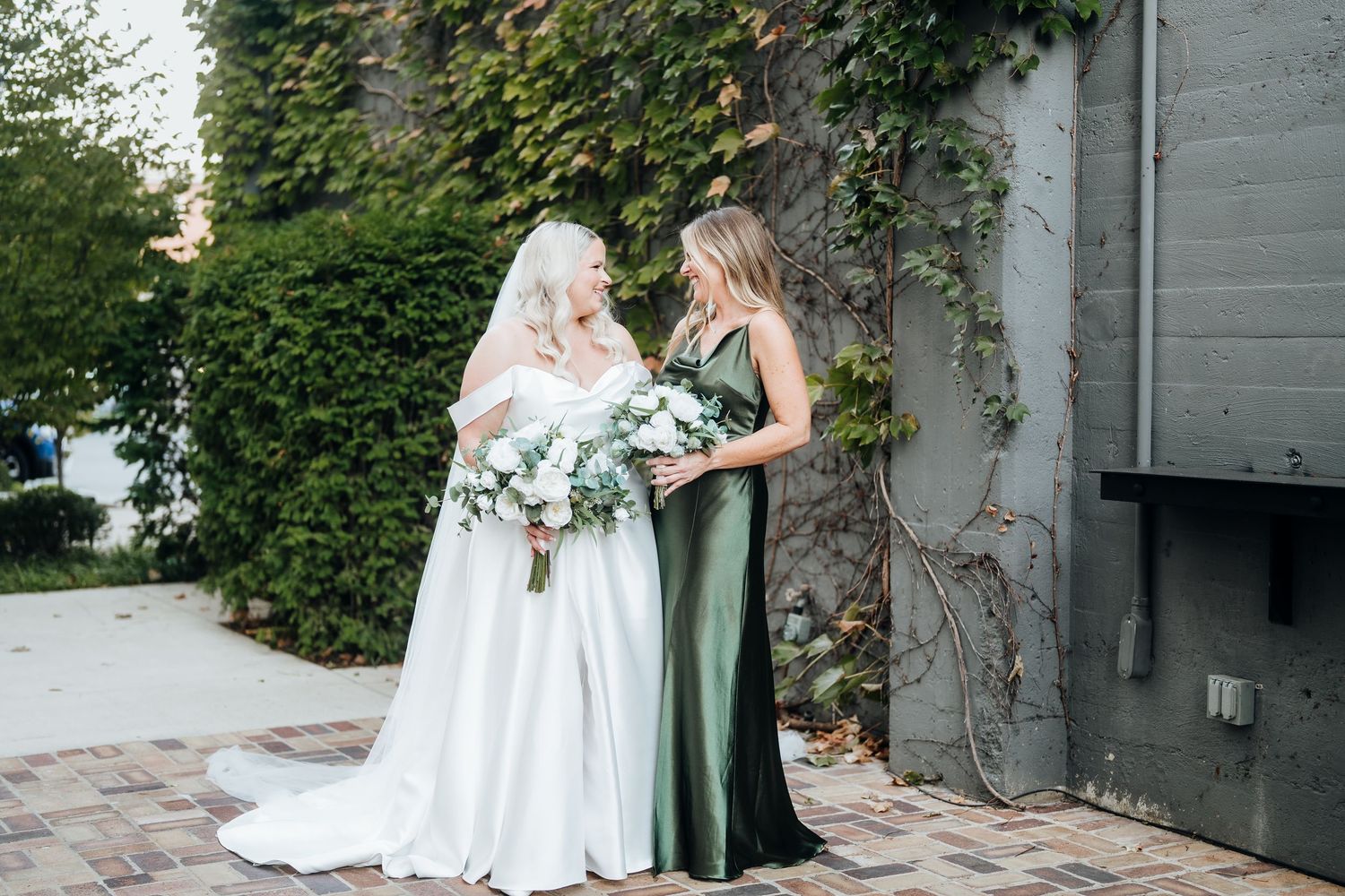 Wedding couple poses against an ivy-covered wall in an outdoor garden setting with natural greenery.