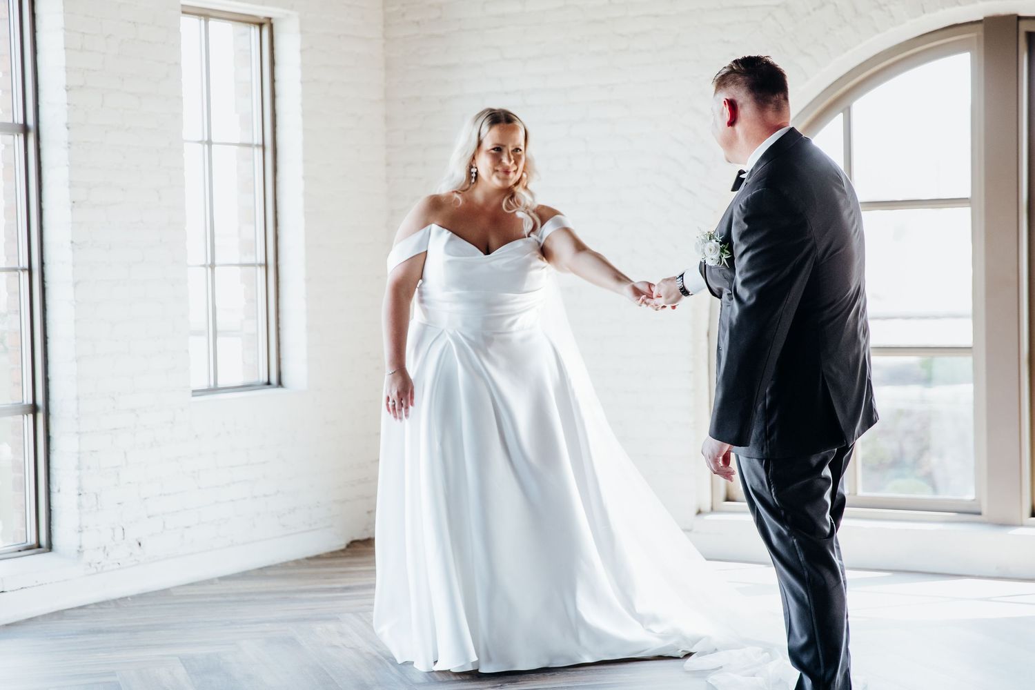 Bride and groom share romantic dance moves in an elegant white brick loft with large windows.