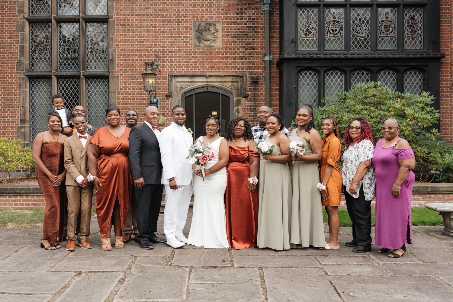 Wedding party poses in earth-toned attire against brick church exterior.