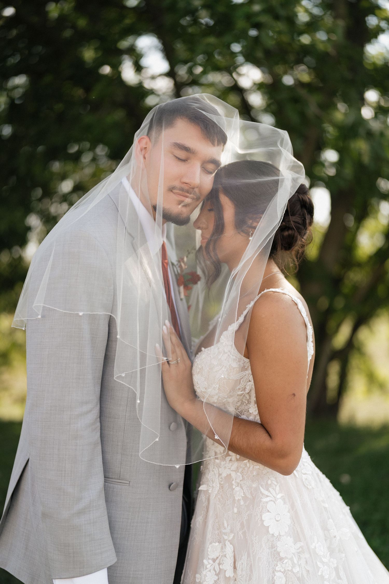 Romantic wedding couple sharing intimate moment under veil in outdoor garden setting.