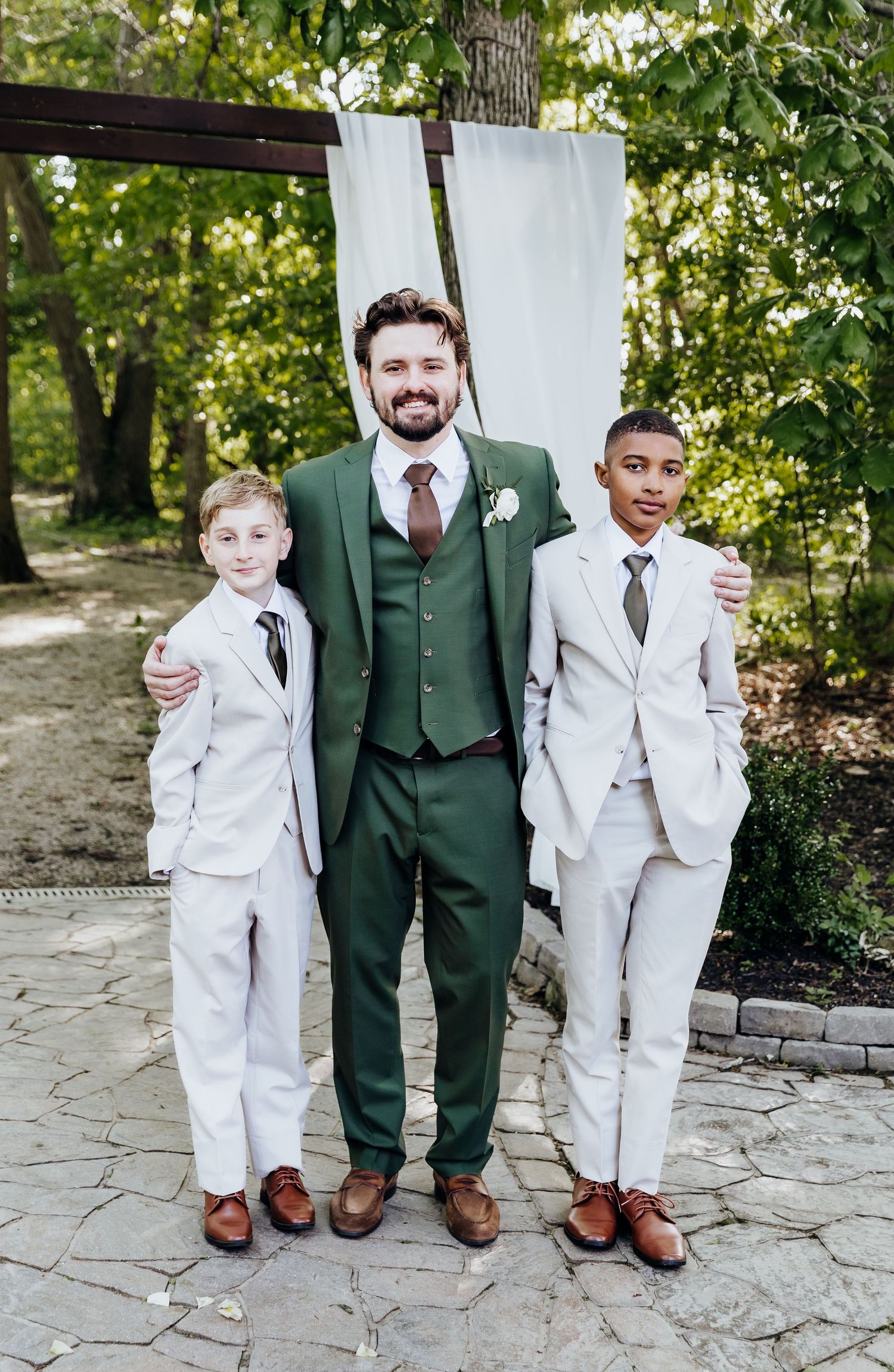 Young ring bearers in white suits pose playfully with groomsman in forest green suit.