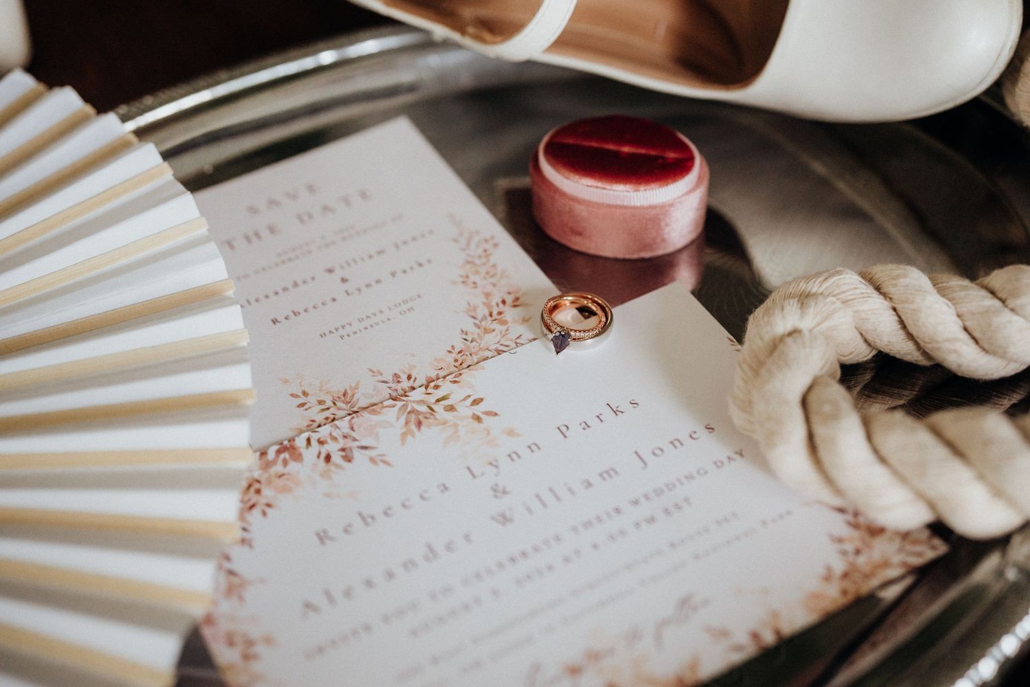Vintage wedding invitation with a decorative paper fan, ring box and delicate details on a textured surface.