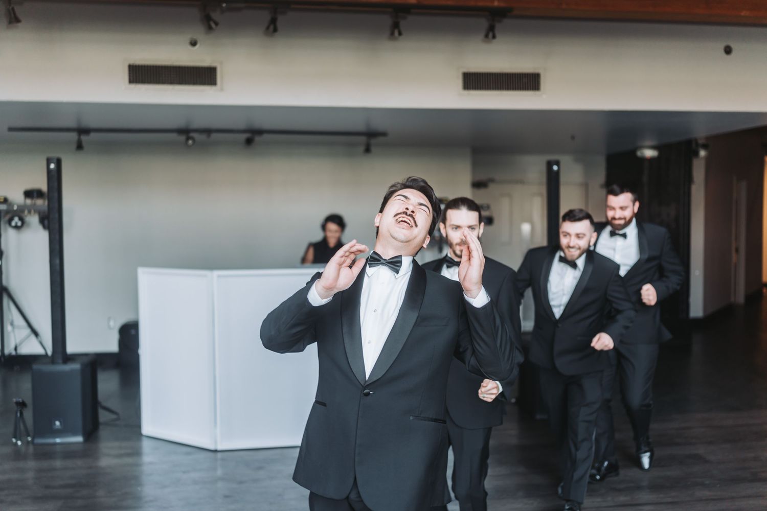 Groomsmen in black tuxedos perform a fun dance routine during wedding reception.