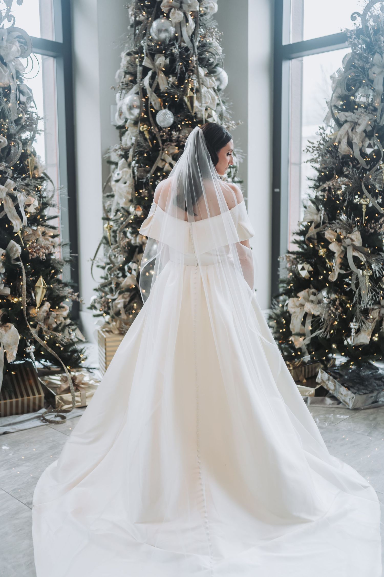 Back view of wedding dress with long train and veil against decorated Christmas trees.