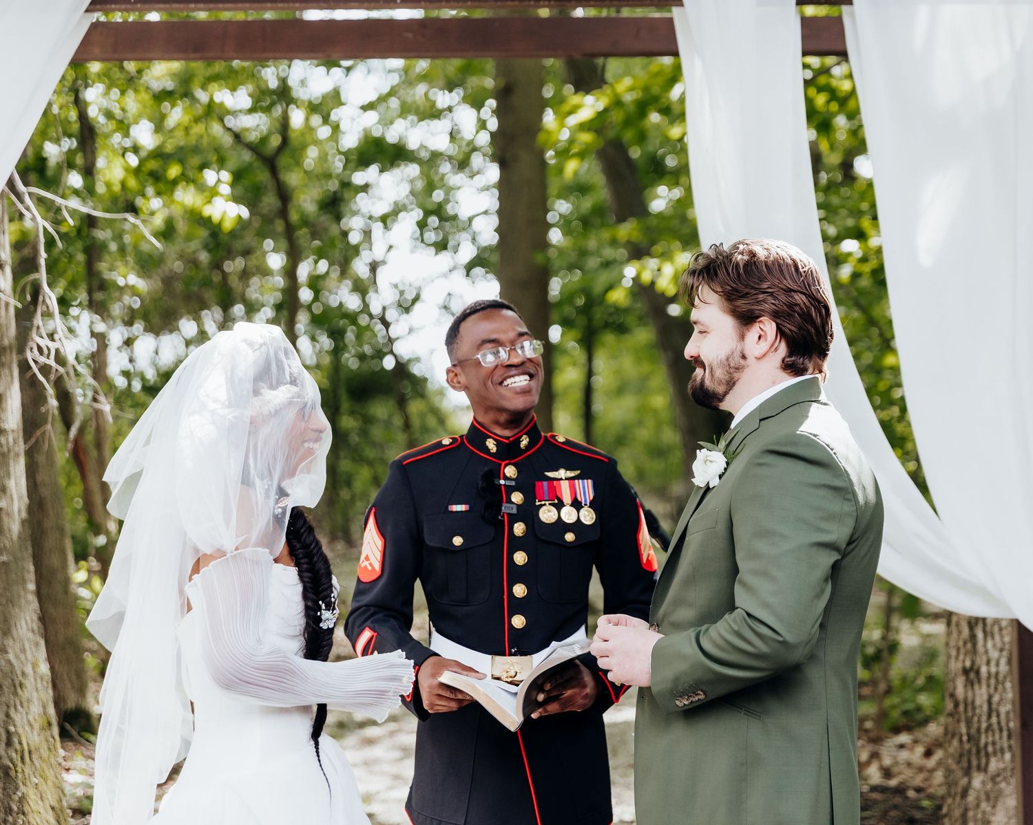 Military wedding ceremony under a white draped arch with service member in dress uniform officiating the vows.