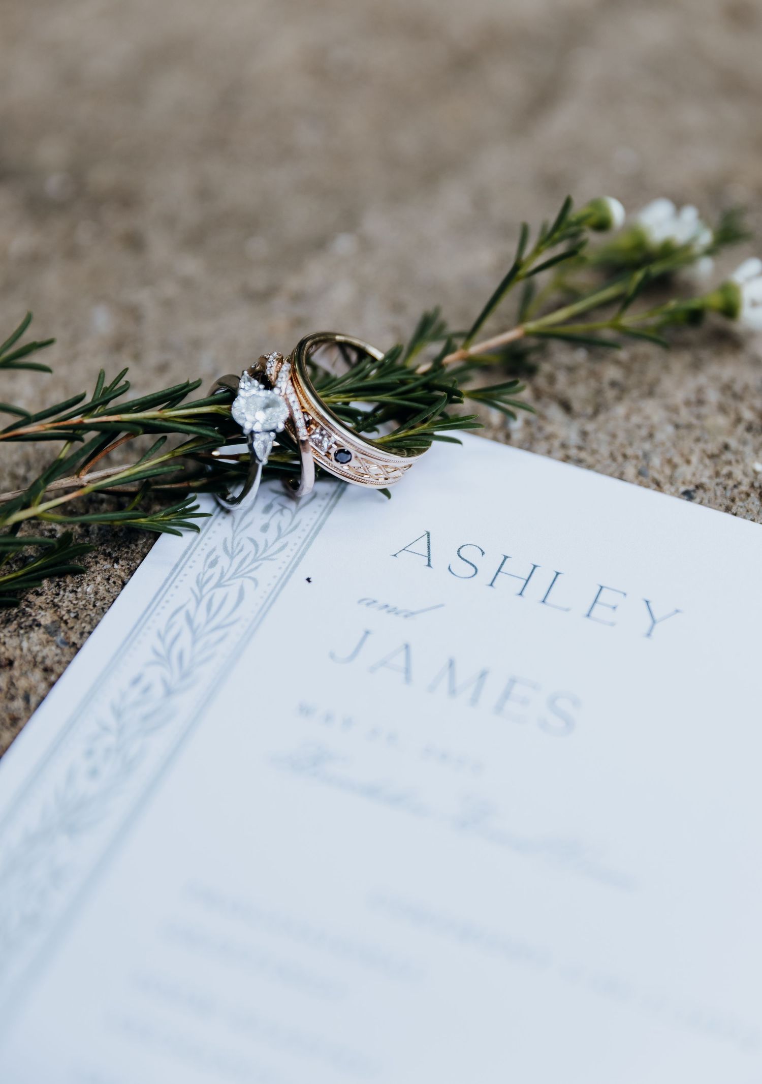 Wedding place cards with names and greenery decorations arranged on textured surface.