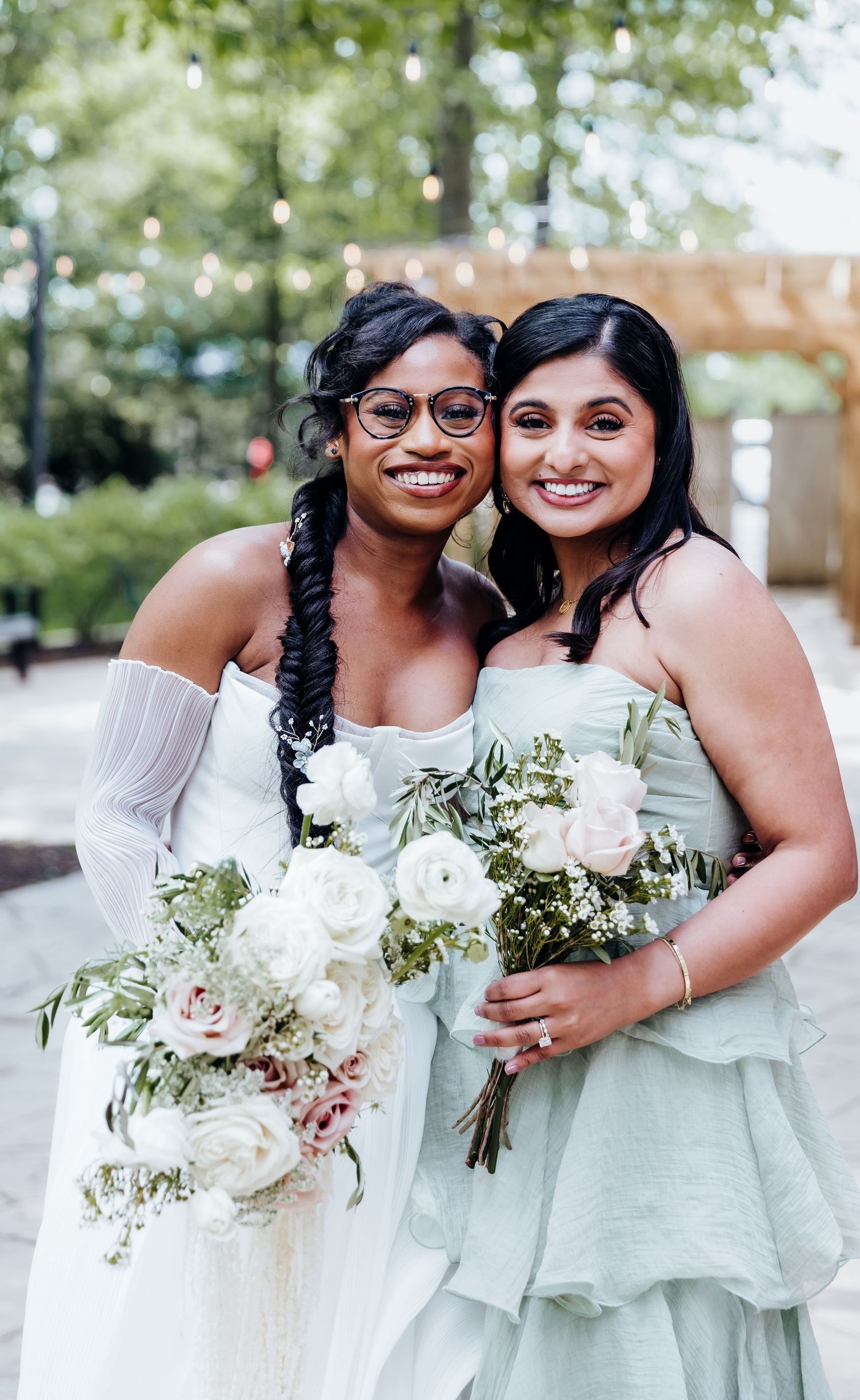 Two bridesmaids in mint green dresses hold white rose bouquets at an outdoor wedding.