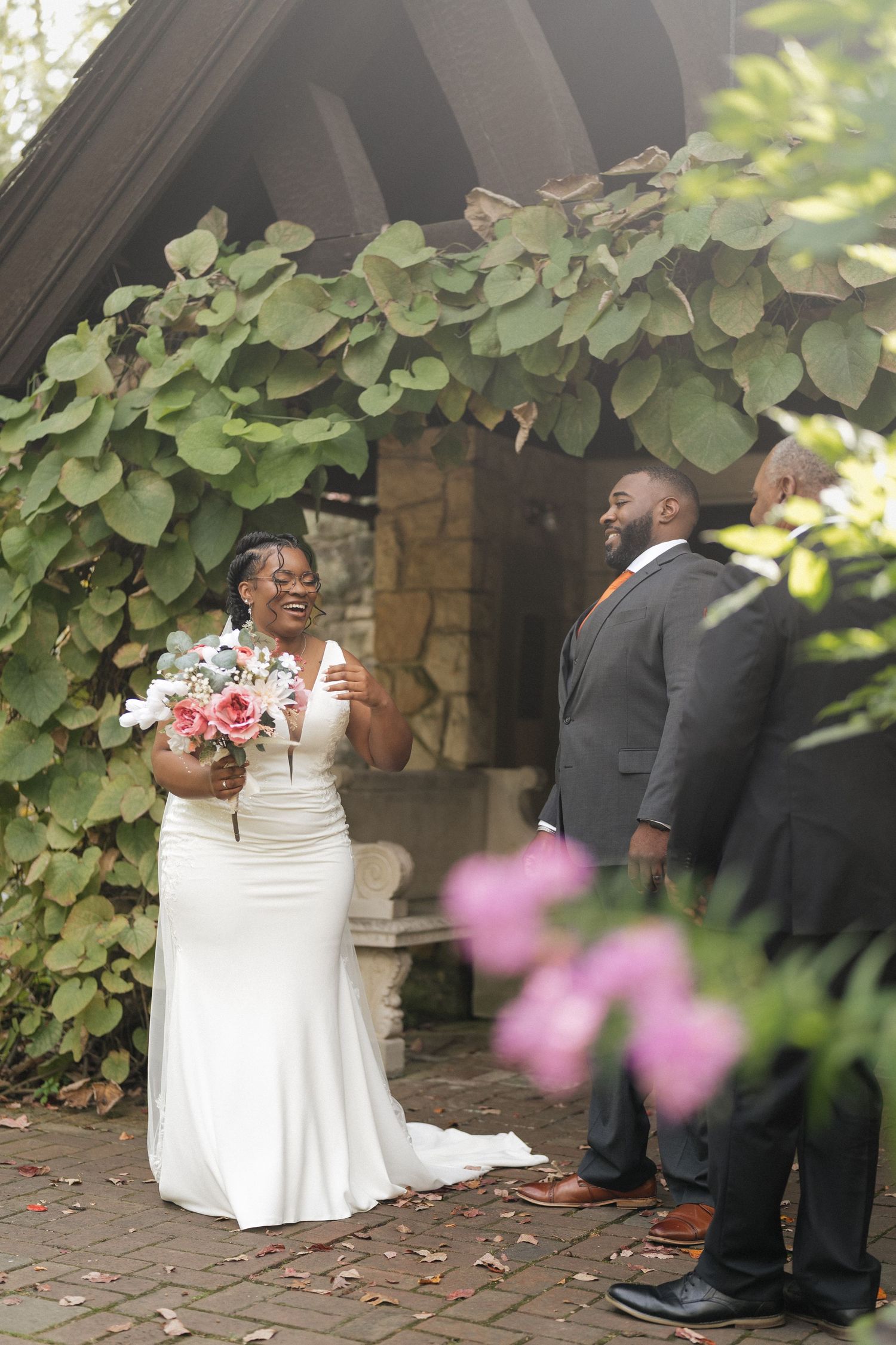 Wedding couple shares a joyful moment under green foliage during their outdoor photo session.