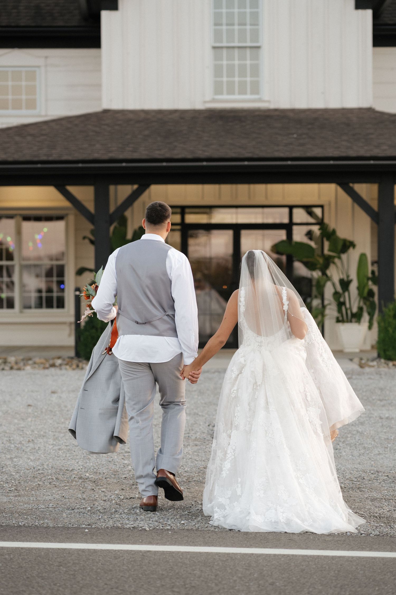 Wedding couple walking along gravel path outside venue building.