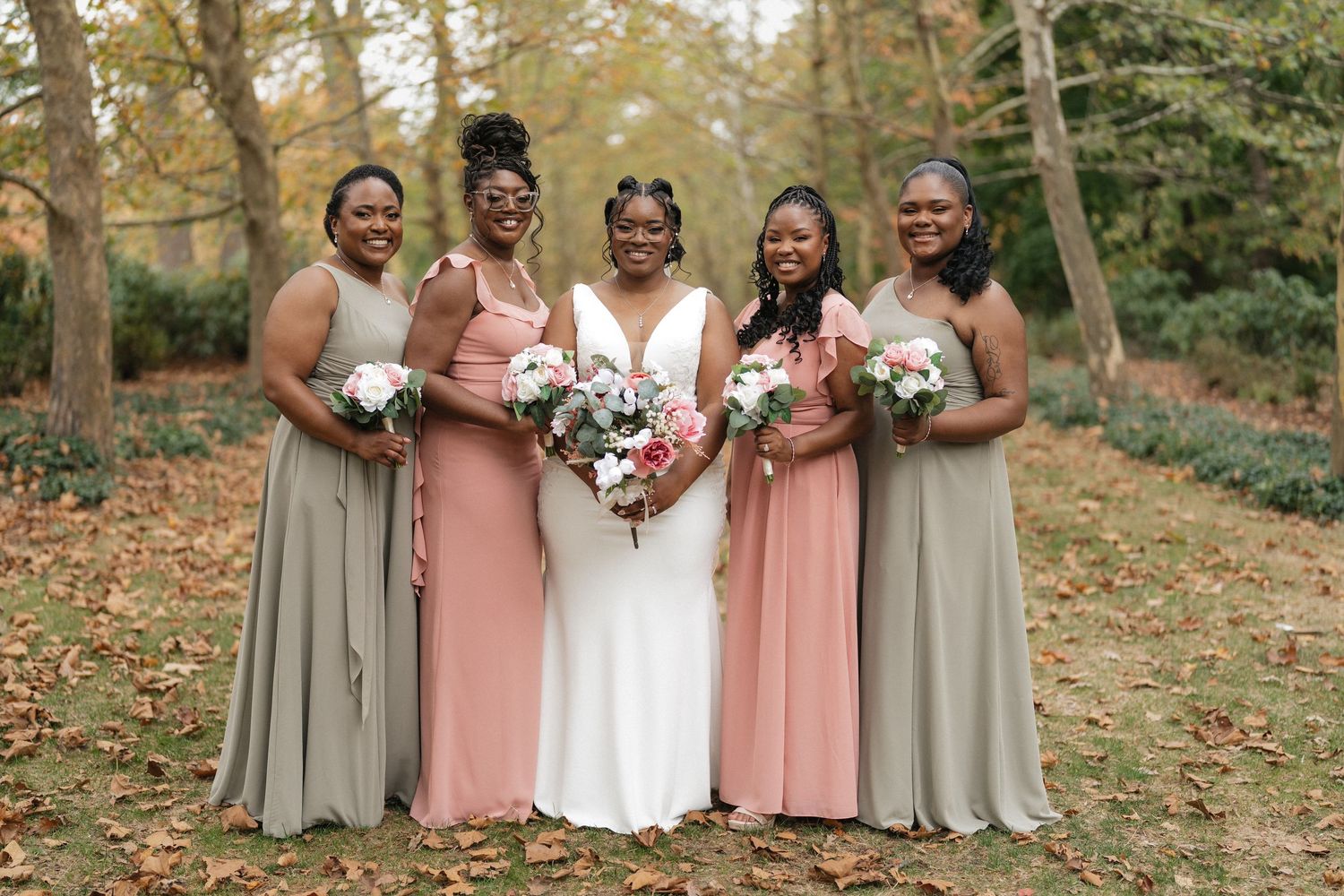 Wedding party in pink and gray dresses standing together on fallen leaves.