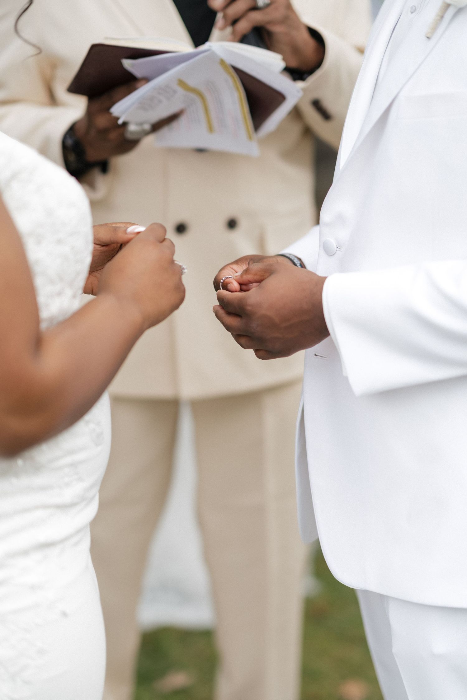 Close-up of hands exchanging rings during a wedding ceremony with white attire.