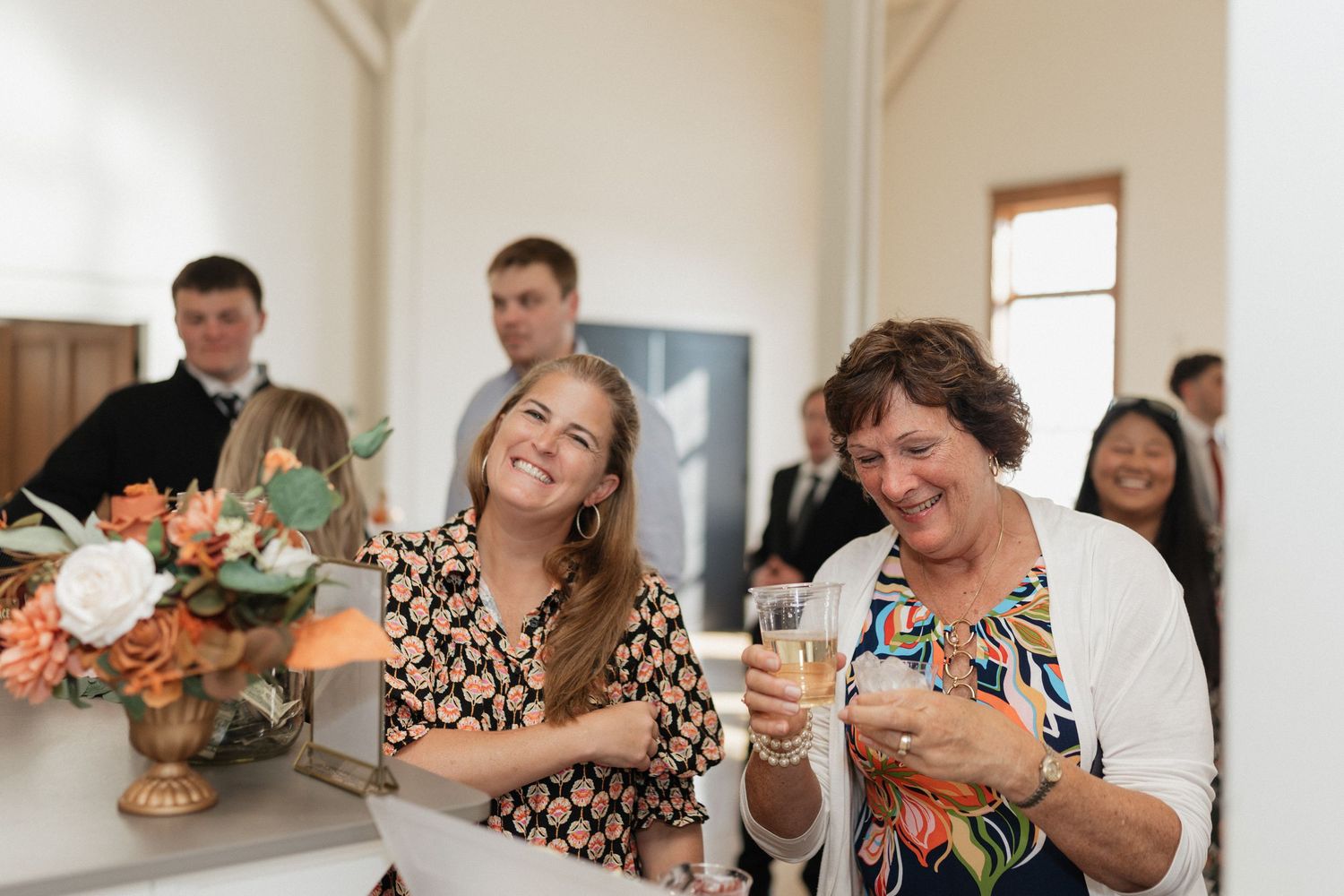 Wedding guests laugh and celebrate while enjoying drinks at an indoor reception.