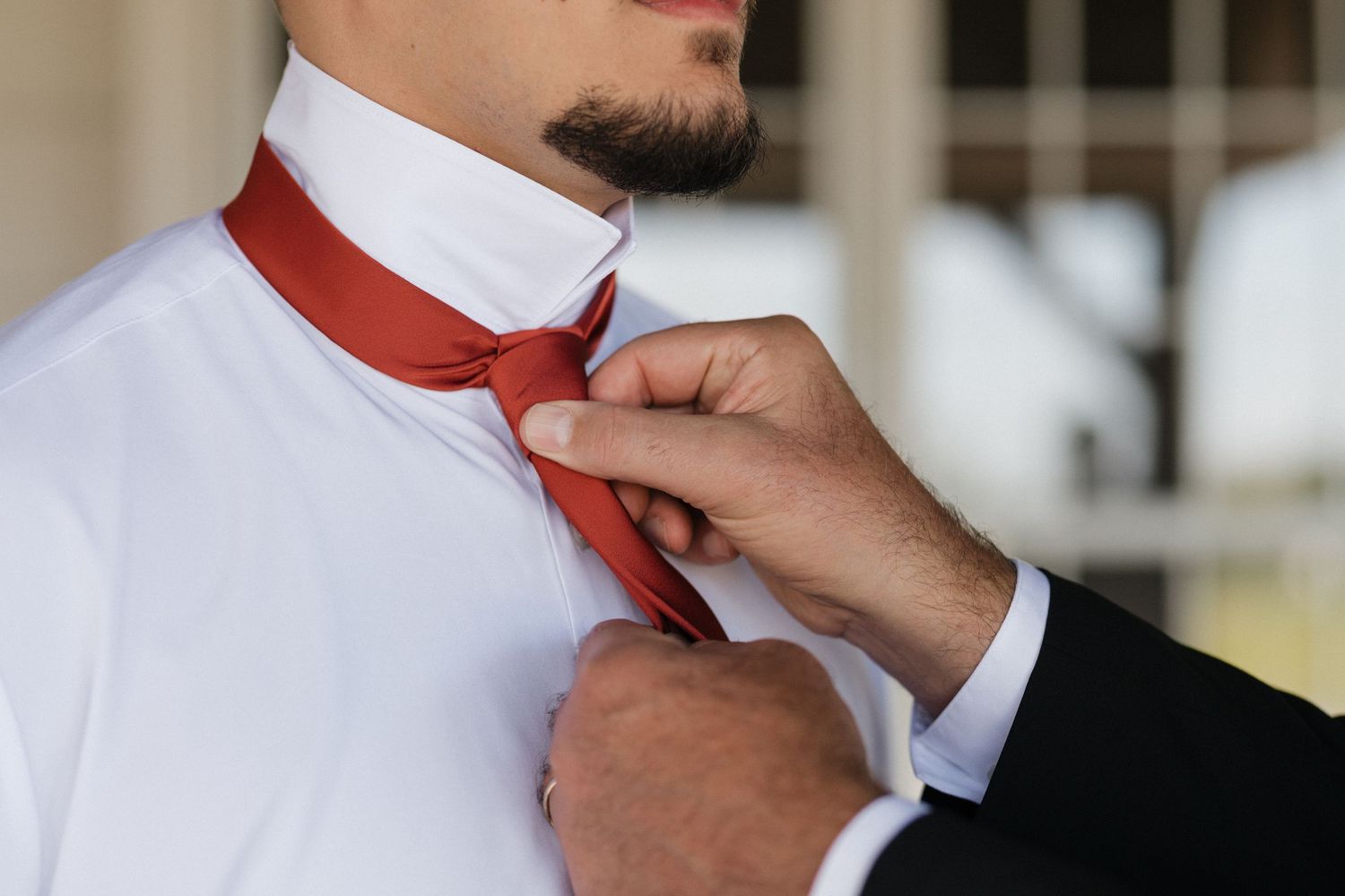 Hands fastening a bright red tie against a crisp white dress shirt.