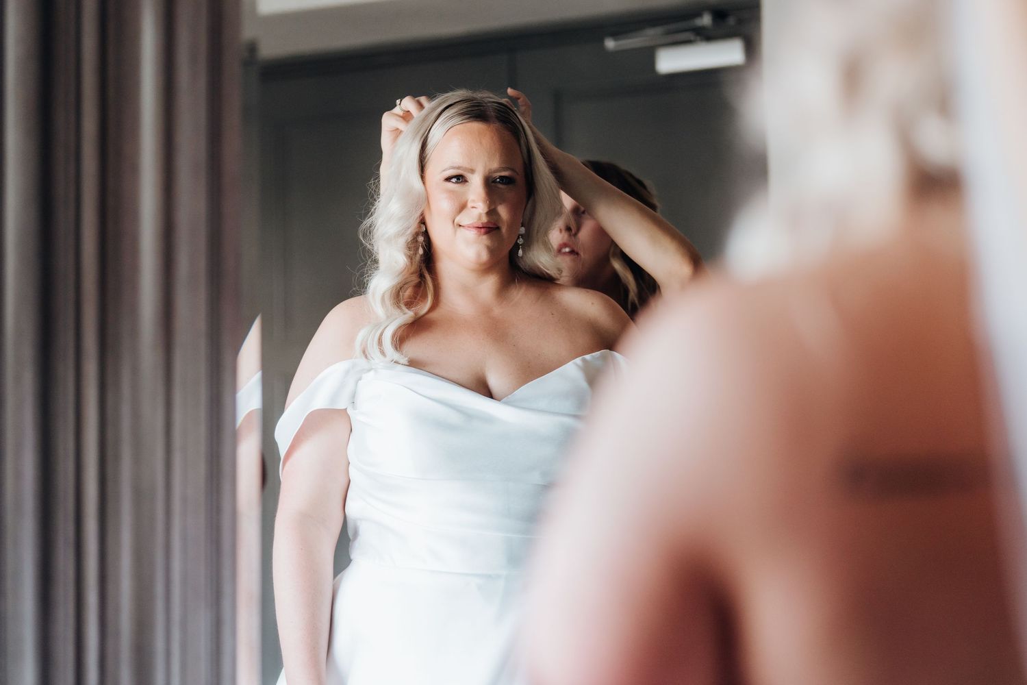 A bride in a classic white wedding gown looks at her reflection in a modern interior setting.