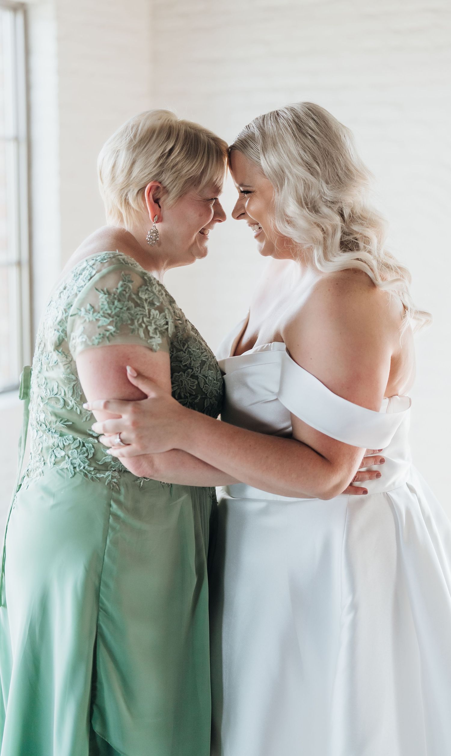 Emotional wedding moment captured in soft light with mint green and white dresses.