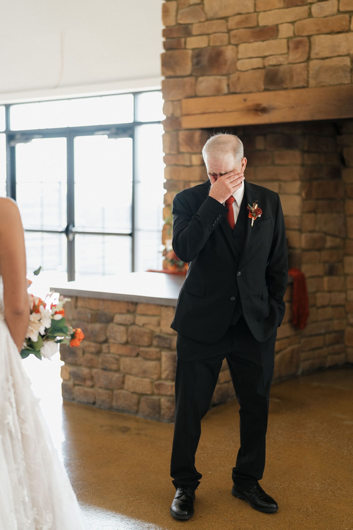 An emotional moment during a wedding as someone wipes away tears near a brick wall.