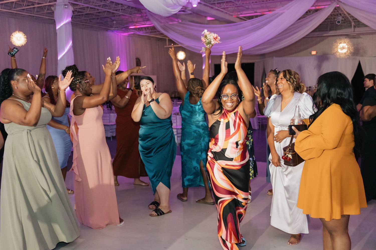 Wedding guests dance joyfully under purple lighting and draped fabric at the reception.