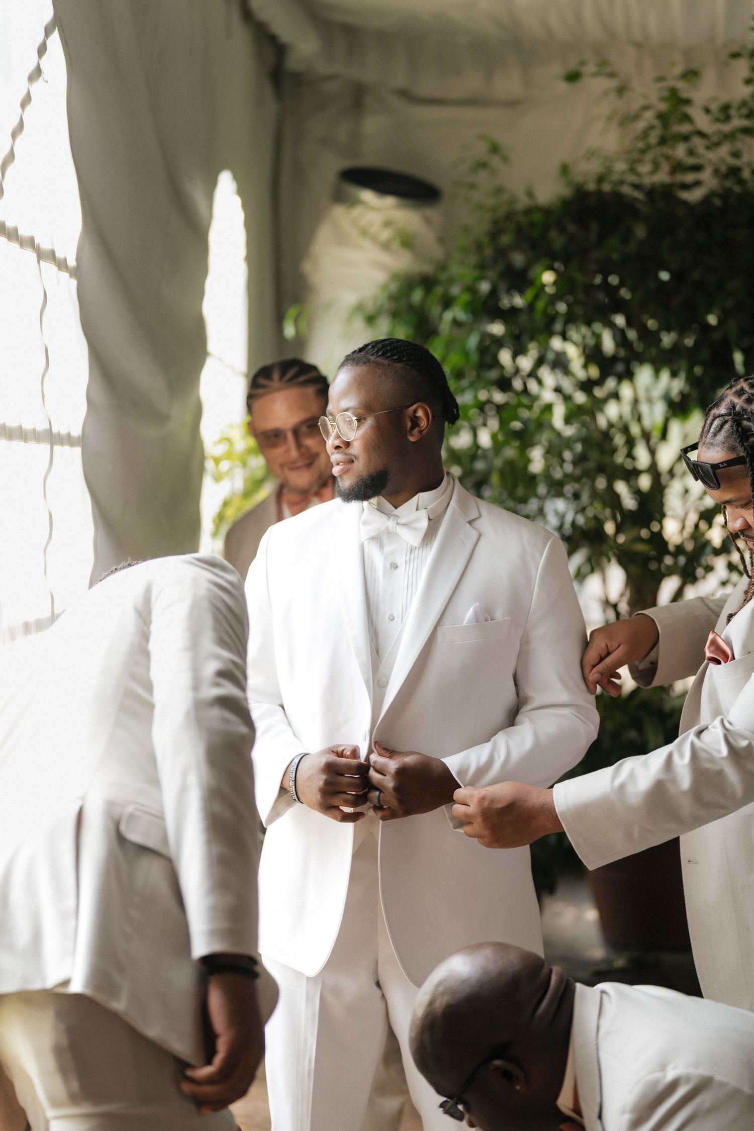 Multiple people dressed in crisp white formal attire gather and interact during a wedding preparation.