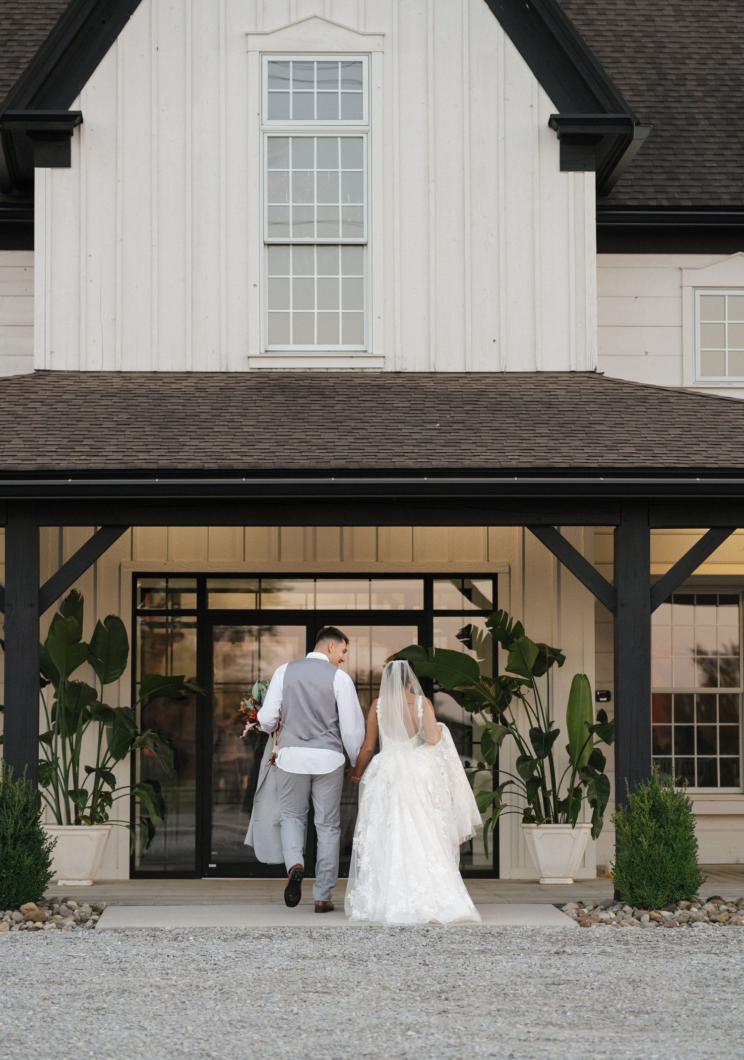 Couple entering modern farmhouse venue with white siding and black trim.