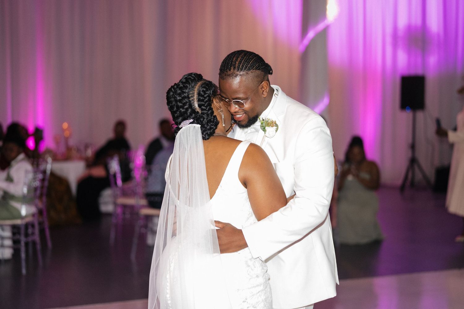 A couple shares their first dance in an elegant reception hall with purple ambient lighting.