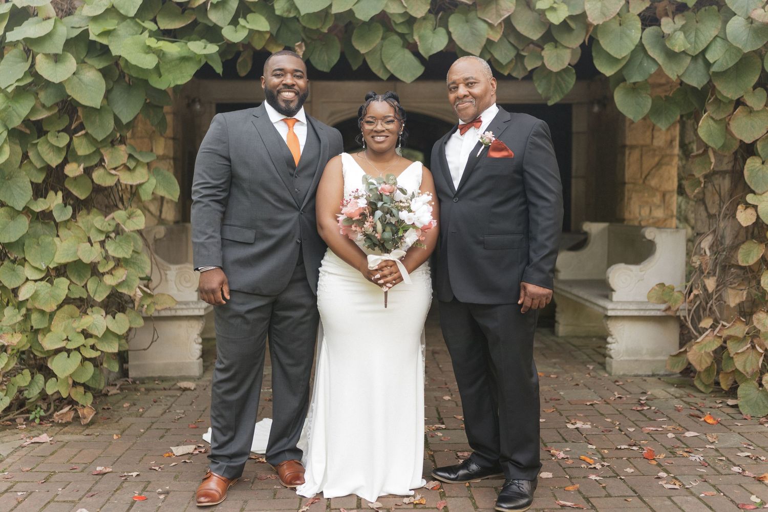 Wedding party poses in front of an ivy-covered stone wall at an elegant outdoor venue.