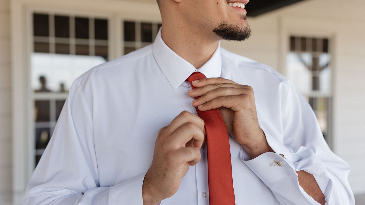 Groomsmen in light gray suits and coral ties share a candid moment outdoors.