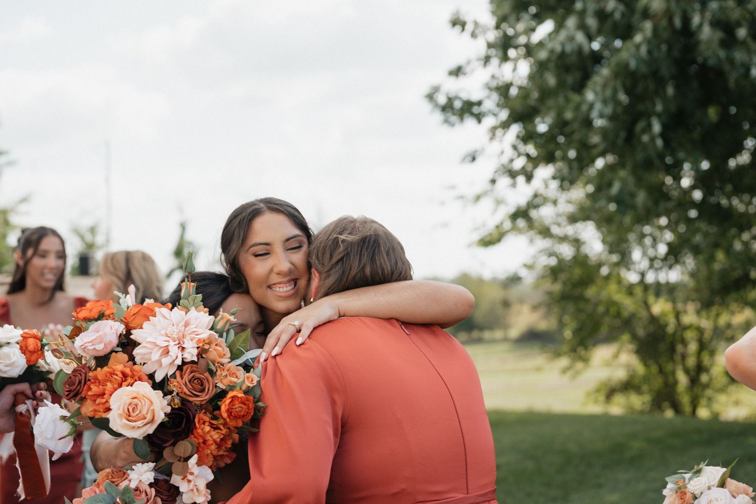 Emotional embrace between wedding attendees next to vibrant orange and white floral arrangements outdoors.