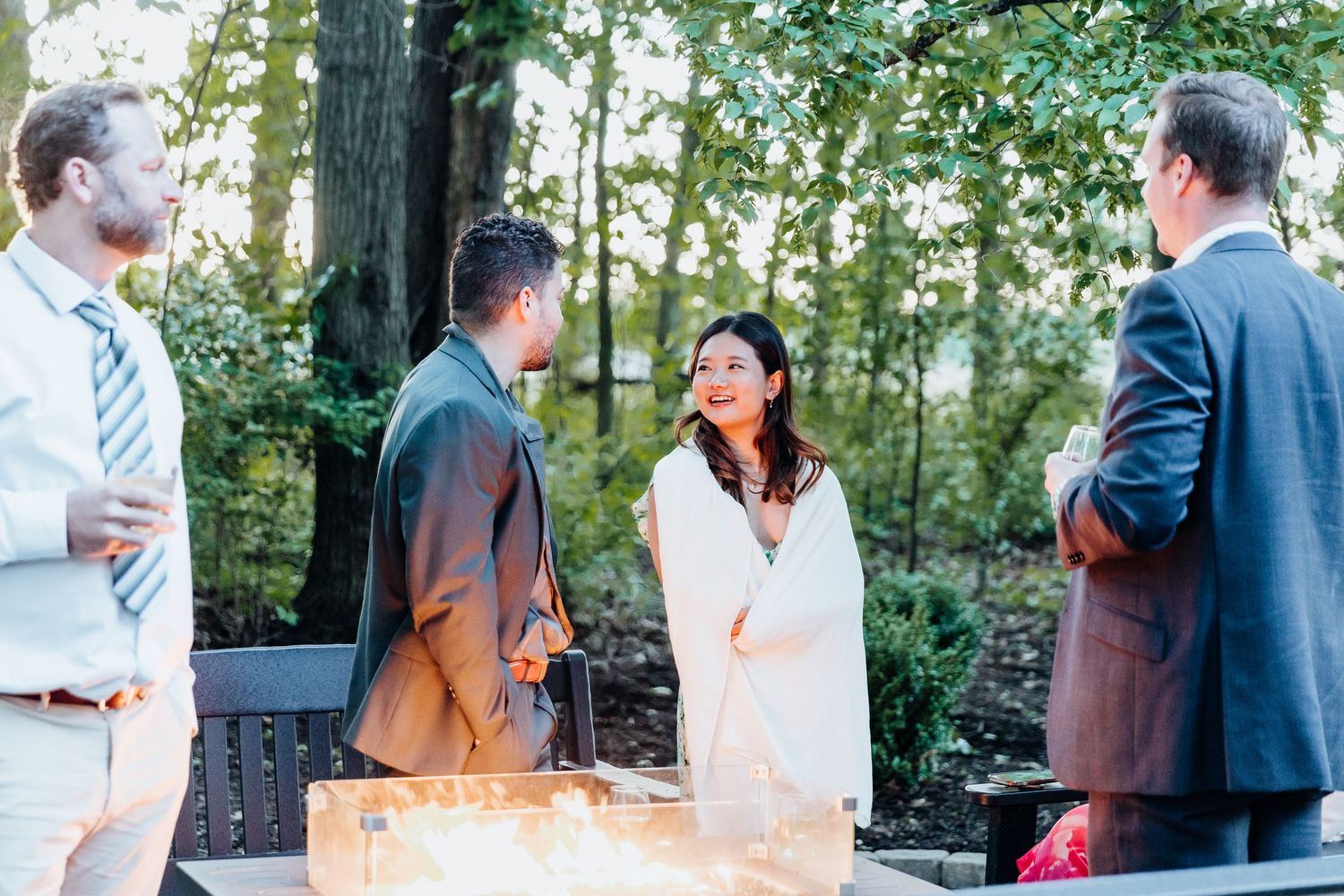 Small group gathering around outdoor fire pit during evening wedding celebration.