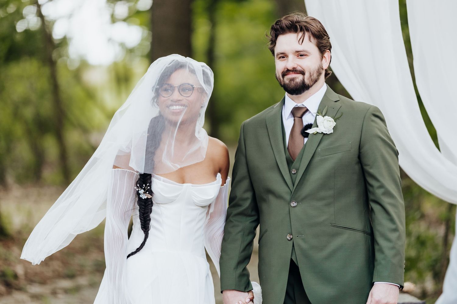 Wedding couple poses in outdoor garden setting with green foliage background.