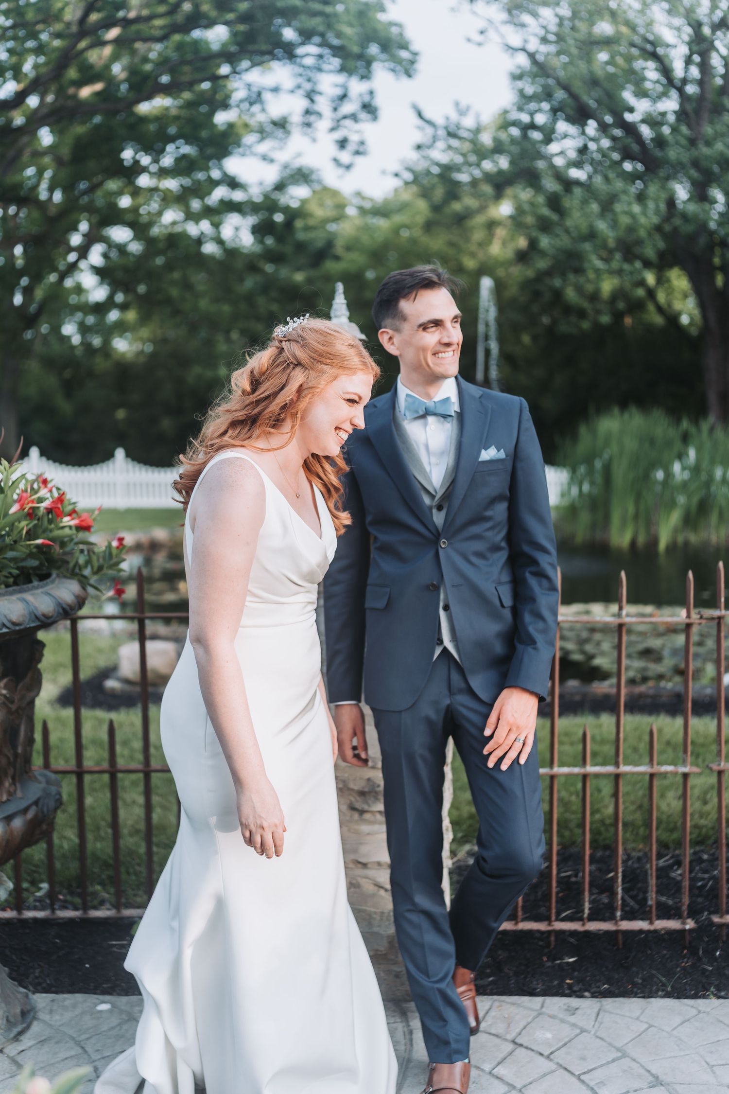 Candid moment of couple in wedding attire laughing together in garden setting with iron fence.