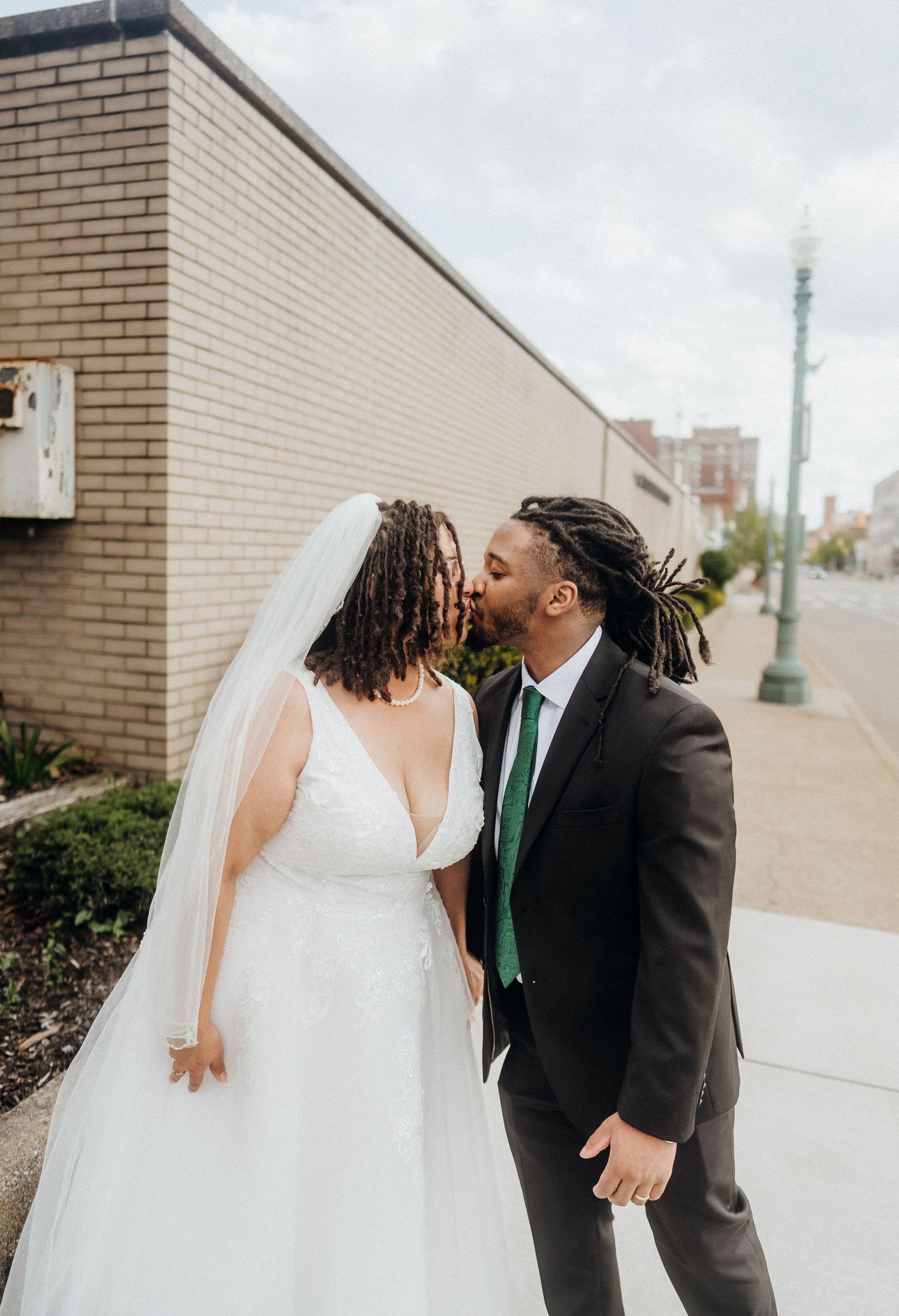 A couple shares a joyful moment in wedding attire against a brick wall backdrop.