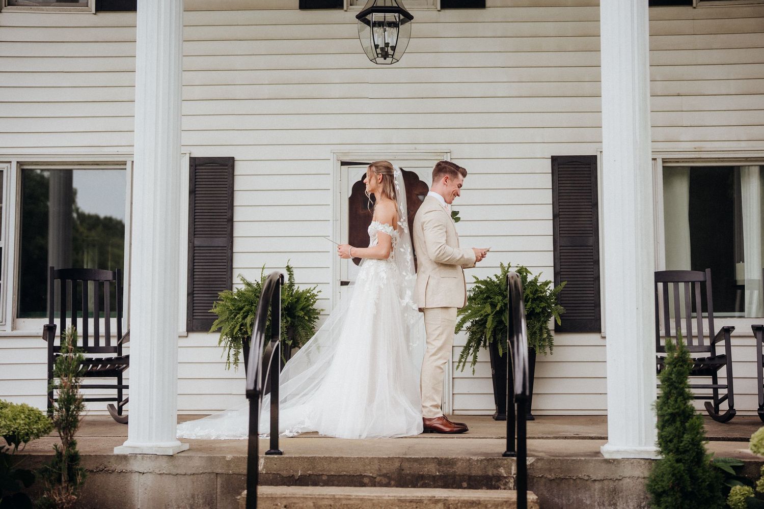 A couple shares a special first look moment on a white colonial porch with rocking chairs.