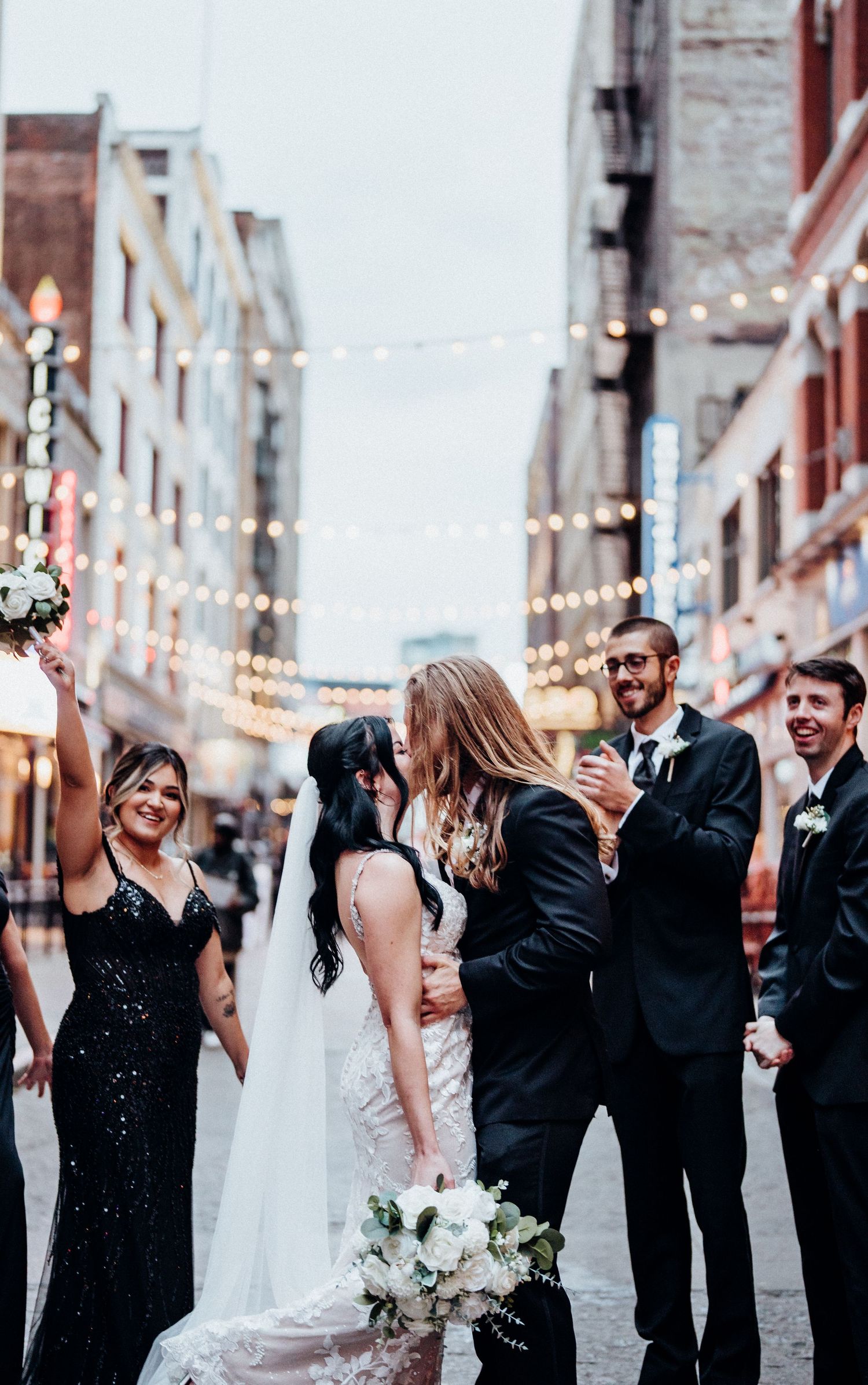 Wedding celebration on a city street with string lights and joyful attendees.