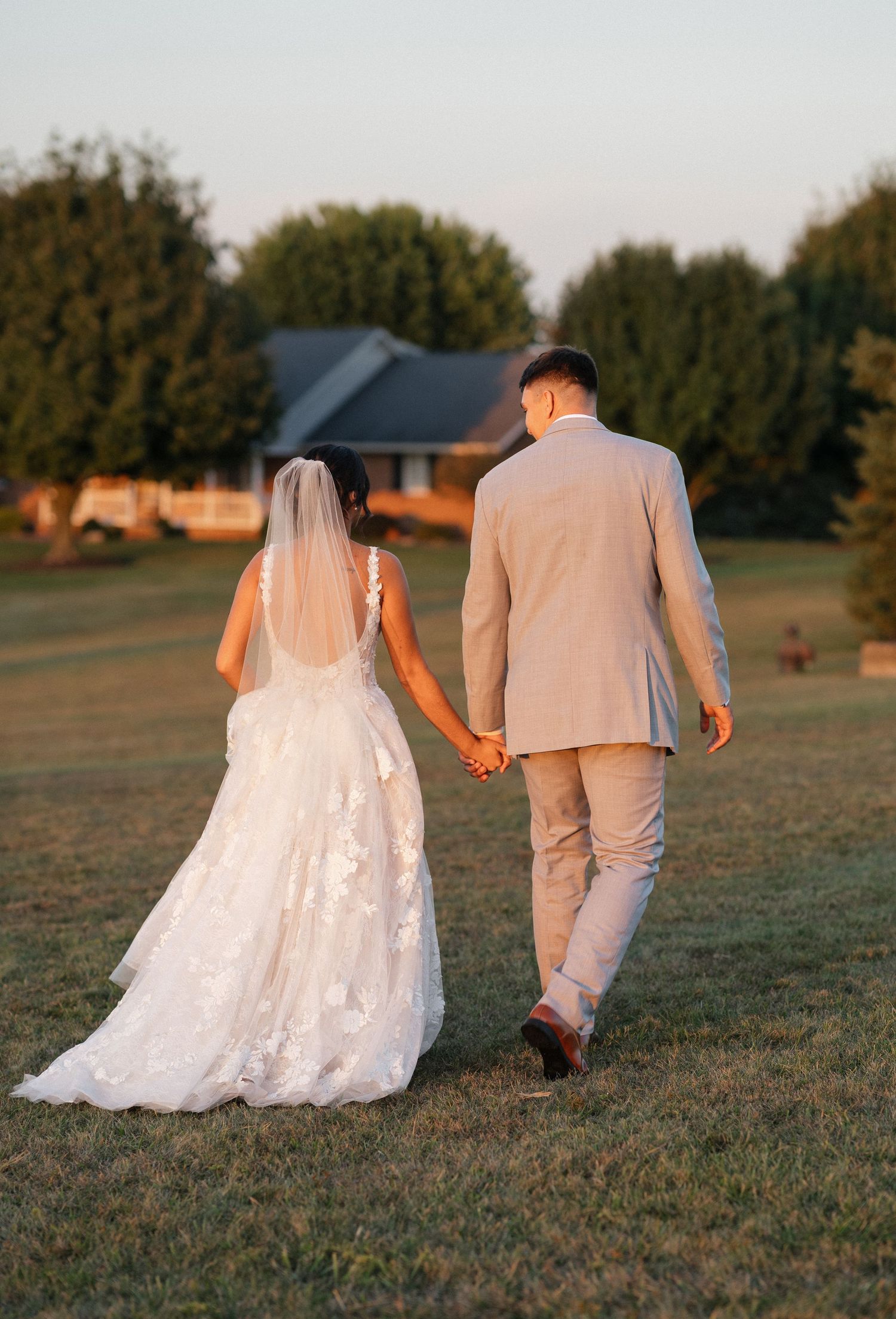 Couple walks hand in hand across field during golden hour wedding photo session.