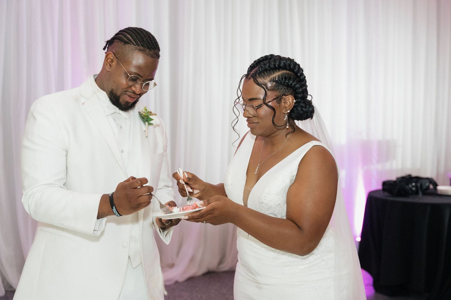 Wedding couple exchanges rings during indoor ceremony with white backdrop.