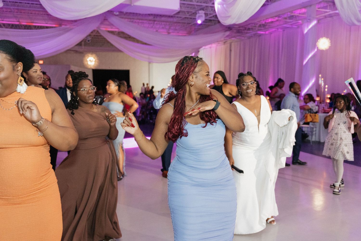 Wedding guests dance and celebrate on a purple-lit dance floor during the reception.